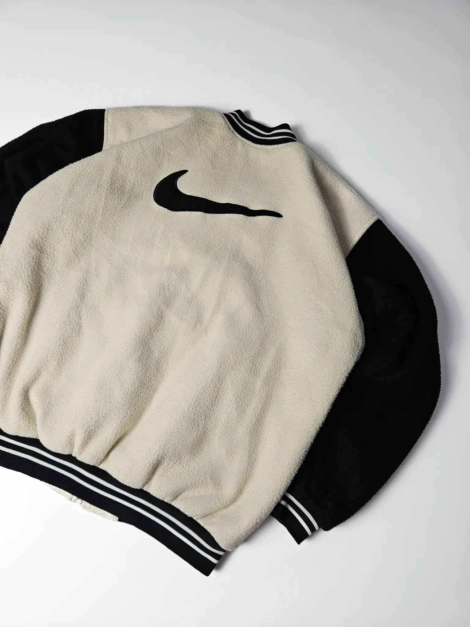 Close-up van groot zwart Nike swoosh logo op beige fleece rug – iconisch jaren 90 varsity jacket design, populair bij streetwear en sportverzamelaars