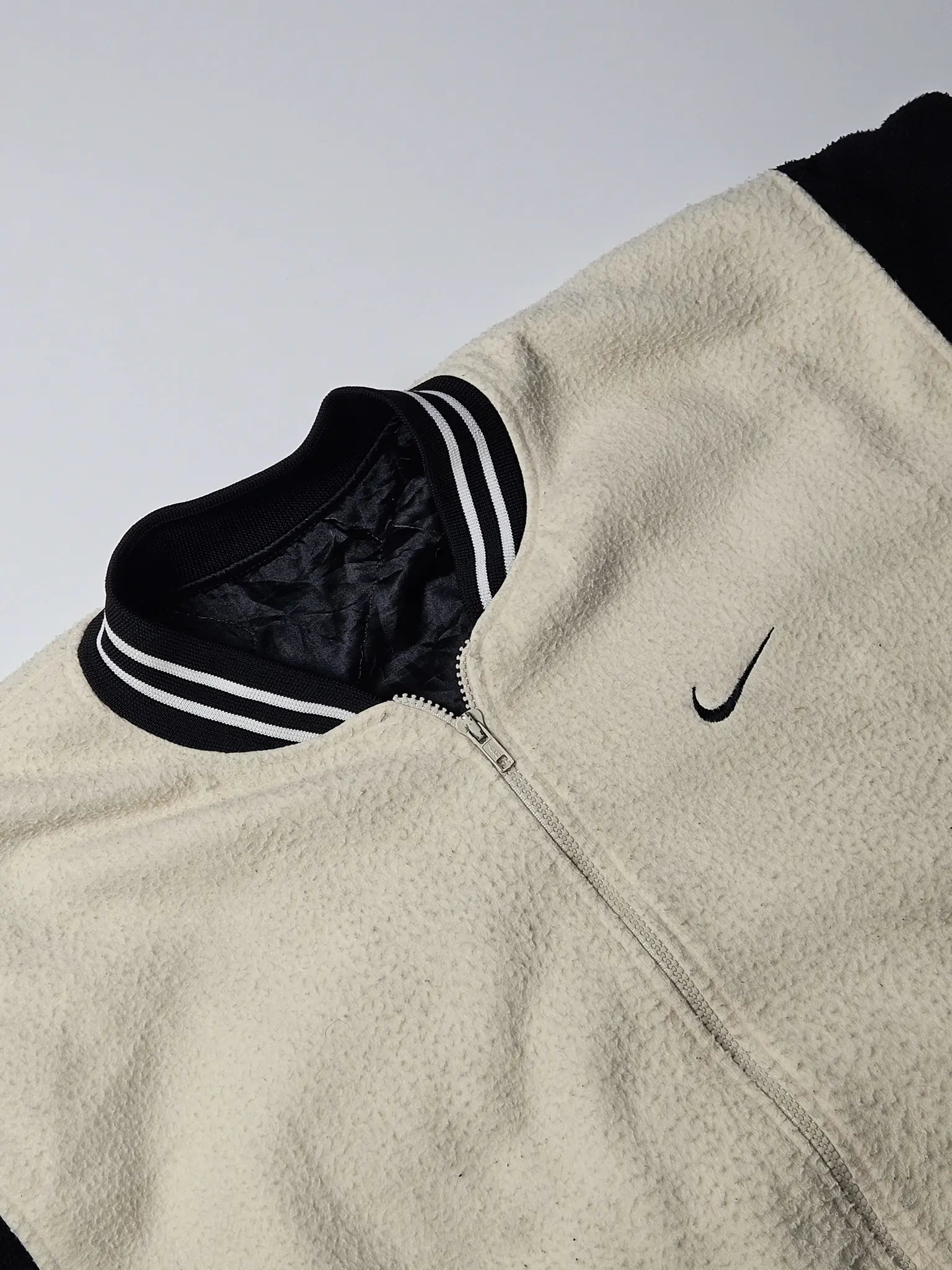 Close-up van beige fleece textuur en zwart geborduurd Nike swoosh logo – jaren 90 vintage varsity jacket, zeldzaam retro sport streetwear
