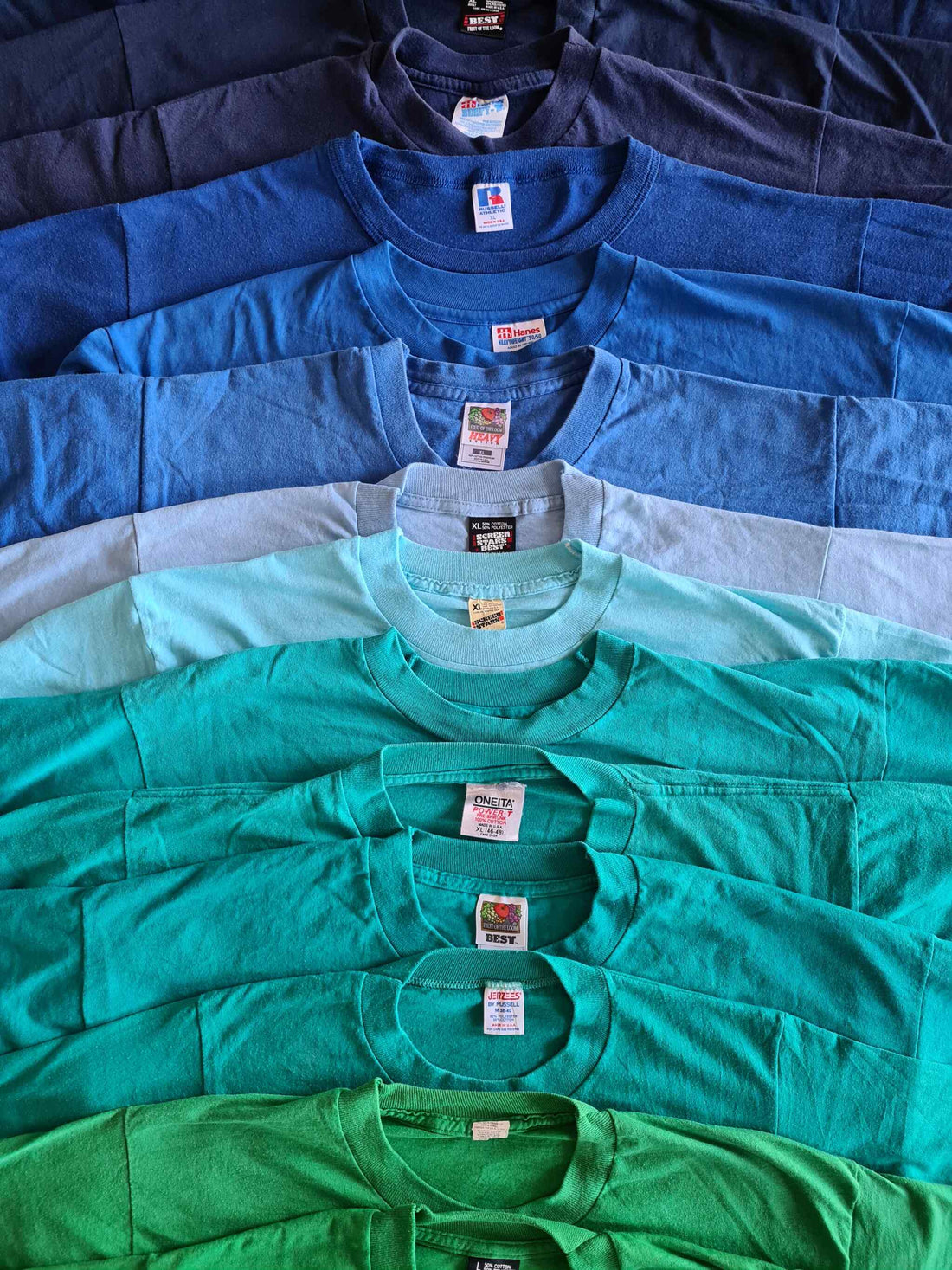 Stapels vintage T-shirts met iconische tags uit de jaren 80 en 90 – onder andere Hanes Beefy-T, Screen Stars, Oneita Power-T, Fruit of the Loom Best en Jerzees.