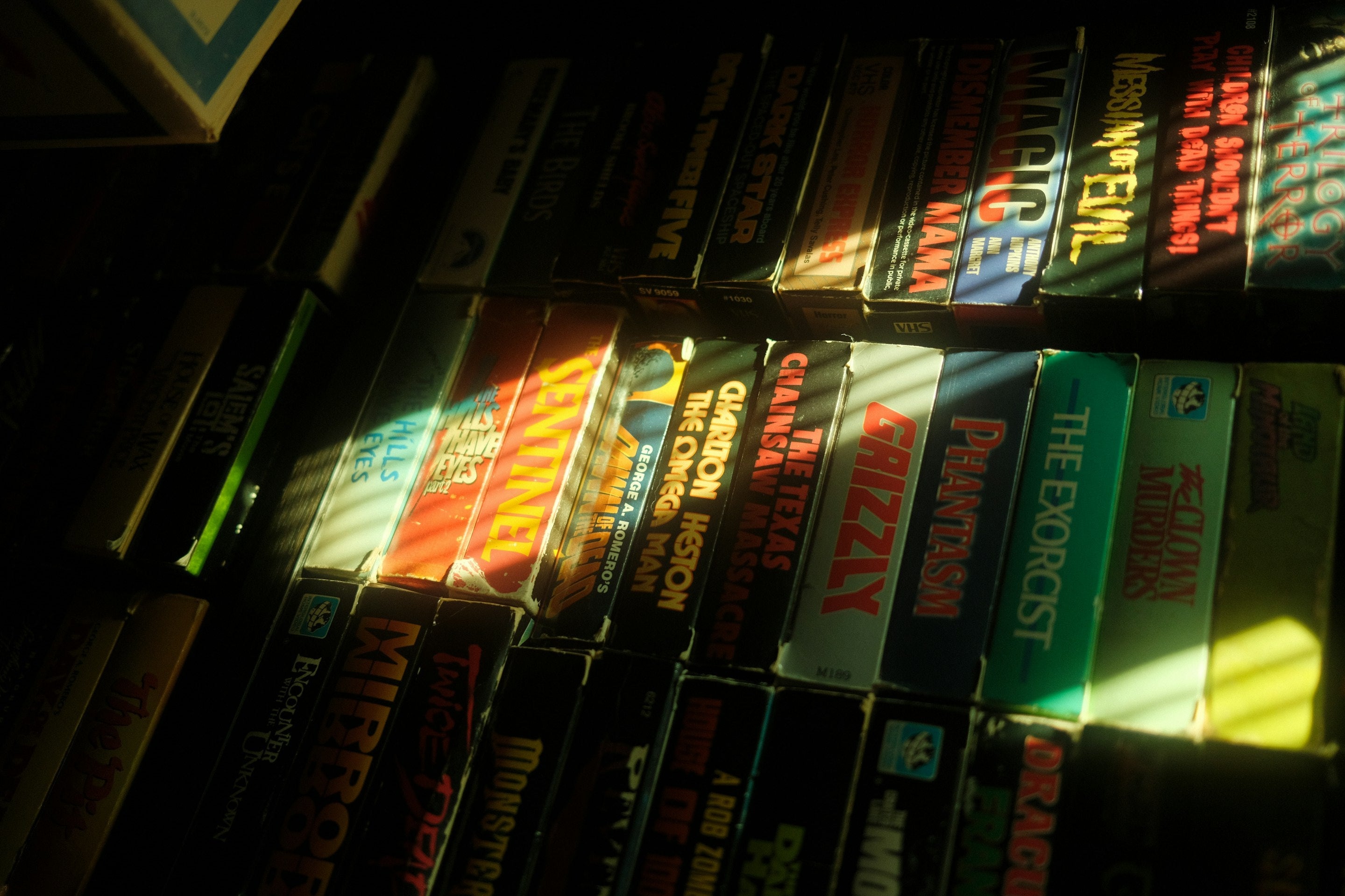 Vintage horror VHS-collectie in zacht zonlicht, met titels als The Exorcist en Texas Chainsaw Massacre – jaren '80 esthetiek in videotheekstijl