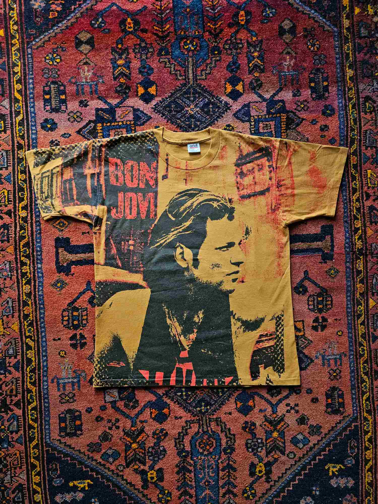 Vintage Bon Jovi T-shirt met all-over print in rood, zwart en beige, liggend op een oosters tapijt met geometrisch patroon – jaren '90 rockband merchandise.