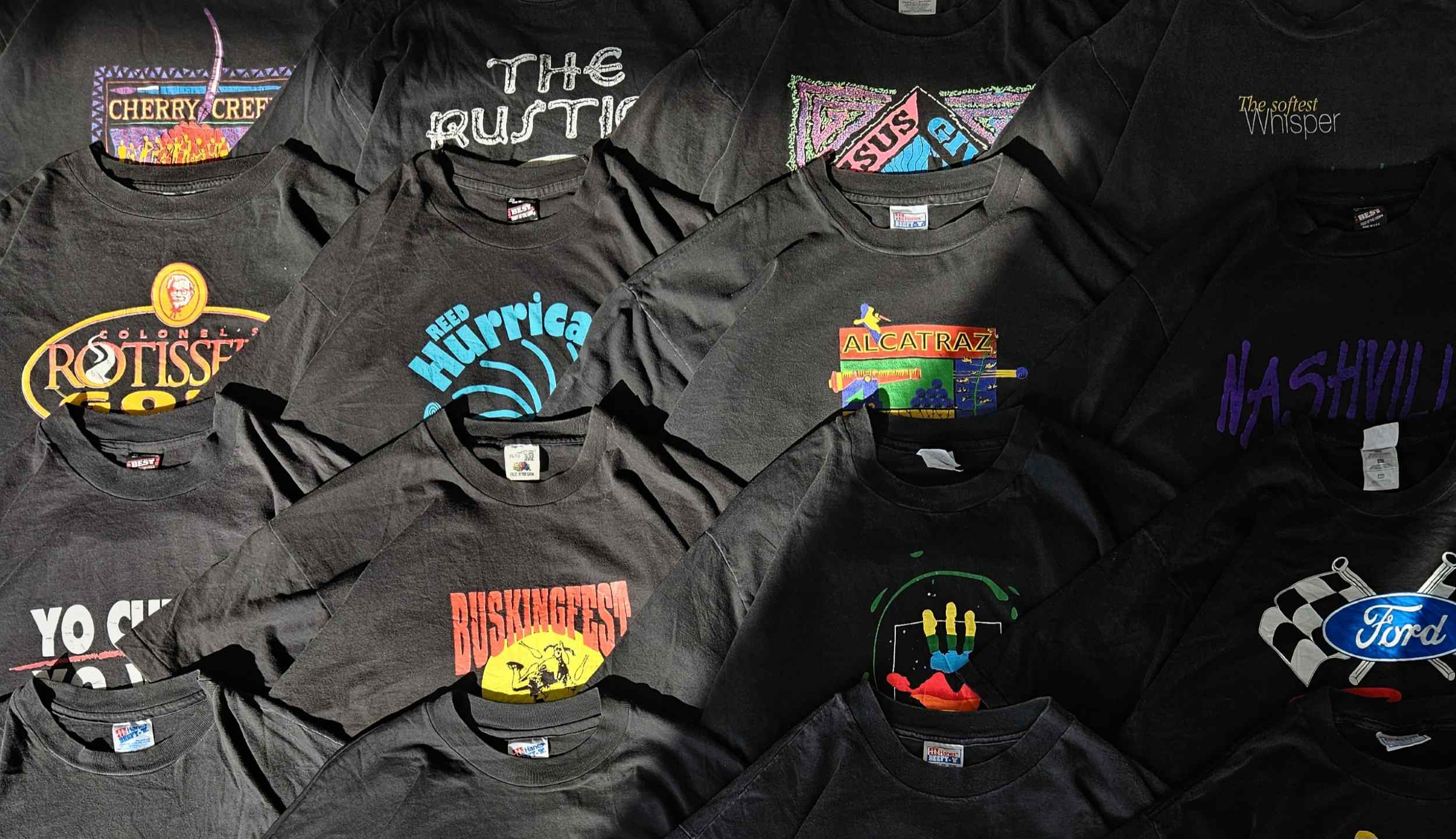 Flatlay van zwarte vintage graphic T-shirts uit de jaren ’90 en 2000s met retro prints, toeristische graphics, sportlogo’s en slogans – onderdeel van de Retro Grafische T-shirts collectie van Slow Fashion Vintage.