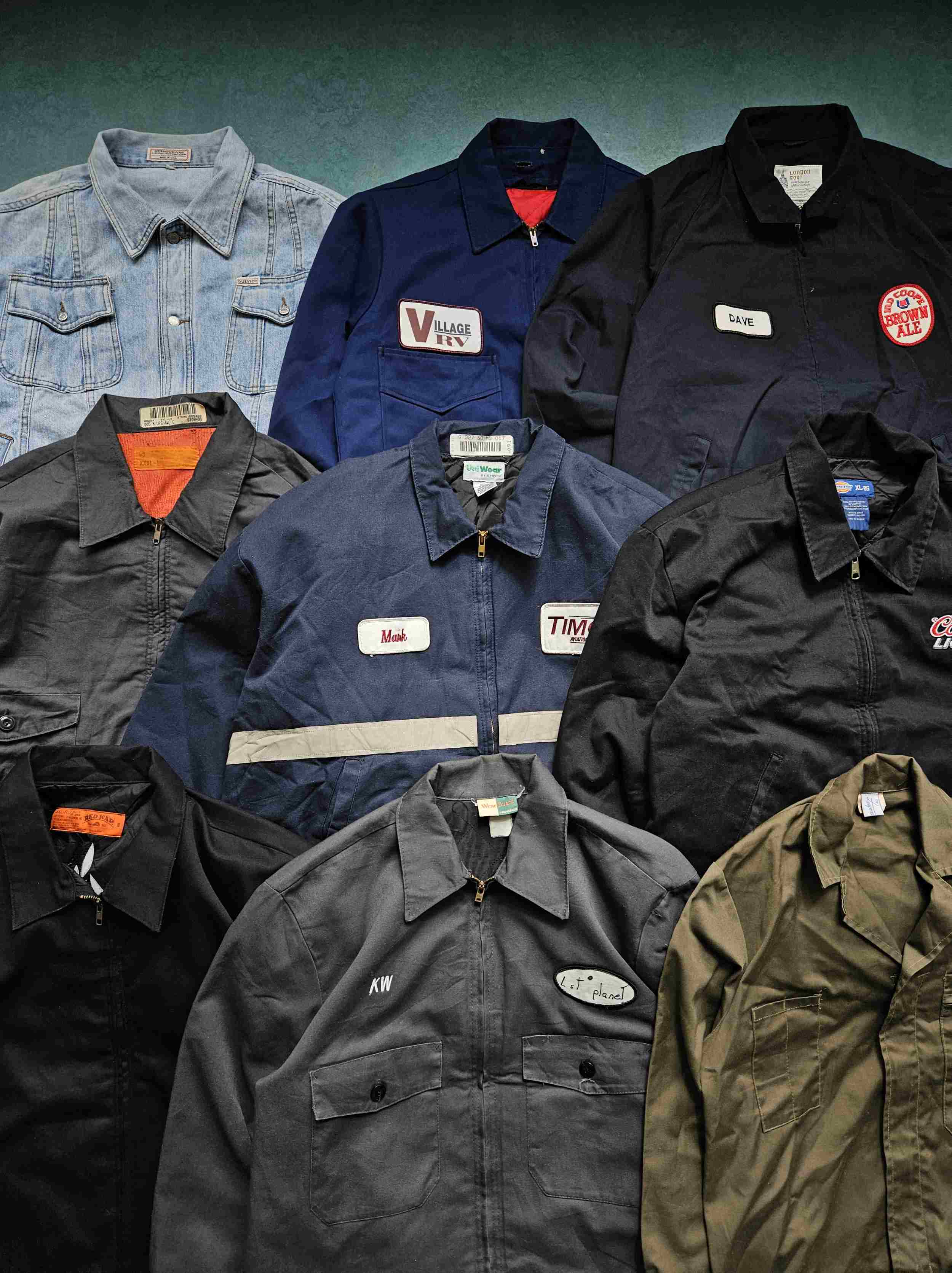 Flatlay van authentieke vintage workwear jassen in verschillende stijlen en kleuren, met patches en naamlabels – waaronder Amerikaanse en Europese utility jackets uit de collectie van Slow Fashion Vintage.