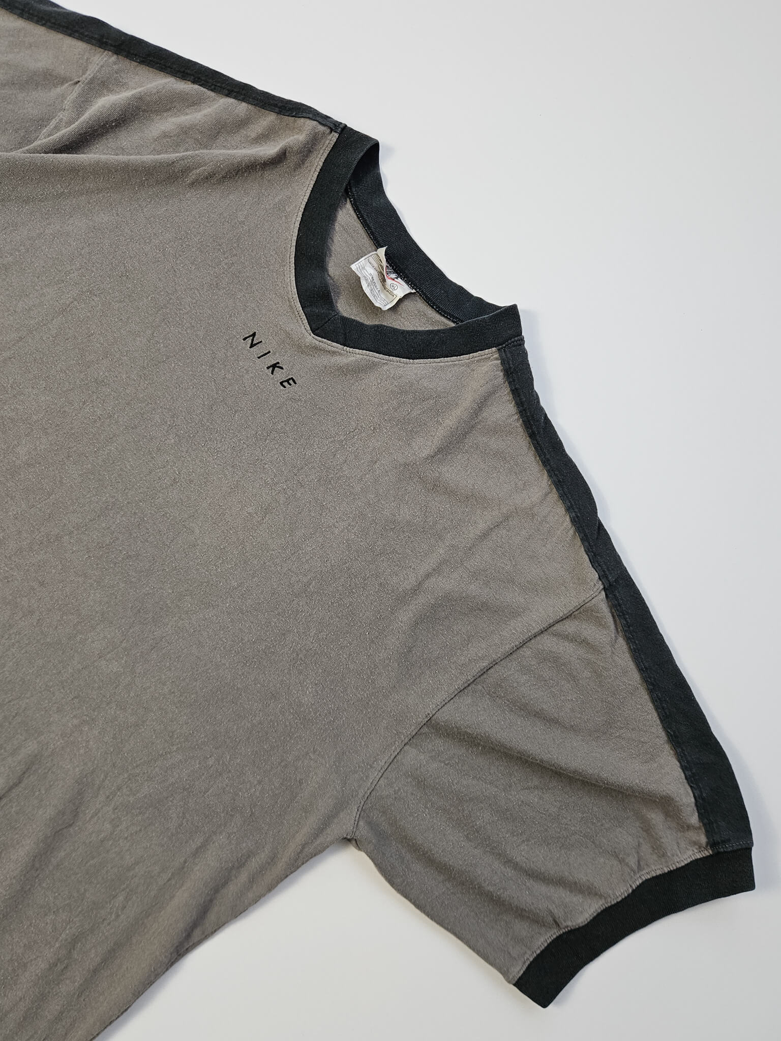 ⦁ Front: 1990s Nike vintage V-neck T-shirt in olijfgrijs met gespaced spellout logo en zwarte schouderpanelen, voorkant flatlay
