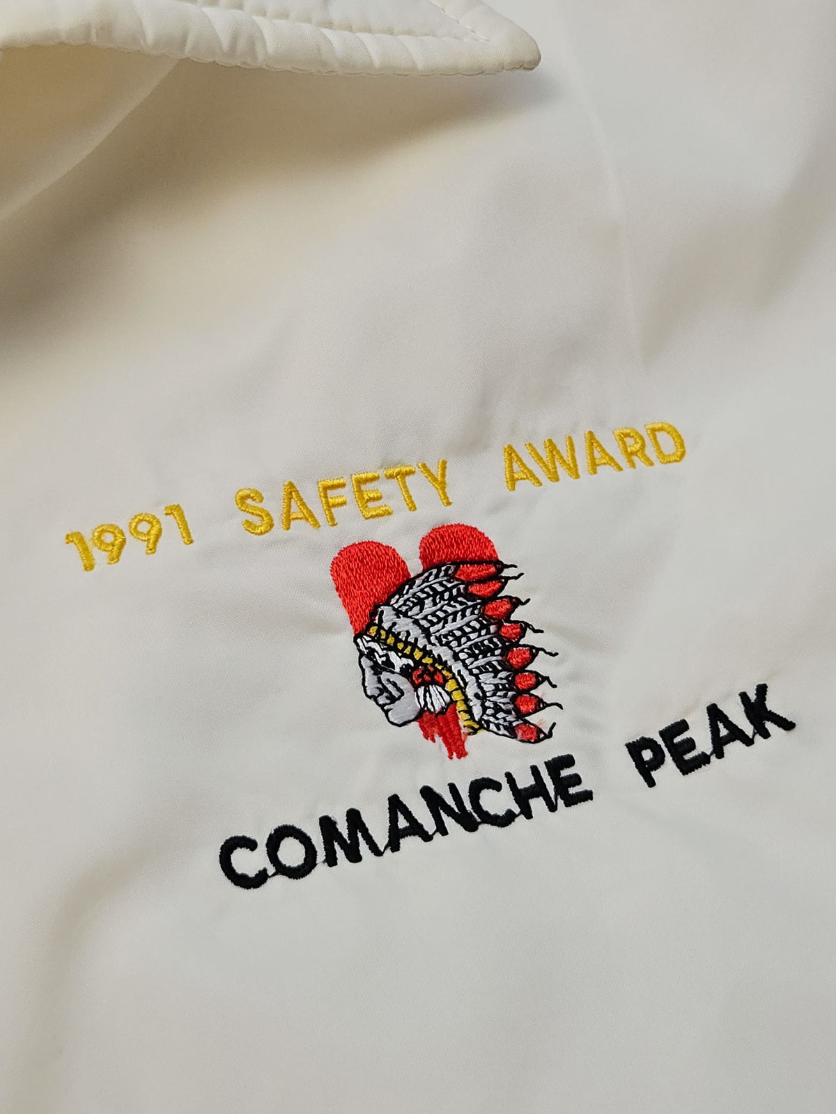 Close-up van het Comanche Peak-borduursel met een verentooi in rood, wit en zwart en de gele tekst ‘1991 Safety Award’.