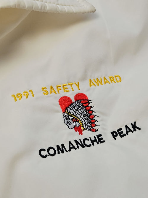 Close-up van het Comanche Peak-borduursel met een verentooi in rood, wit en zwart en de gele tekst ‘1991 Safety Award’.