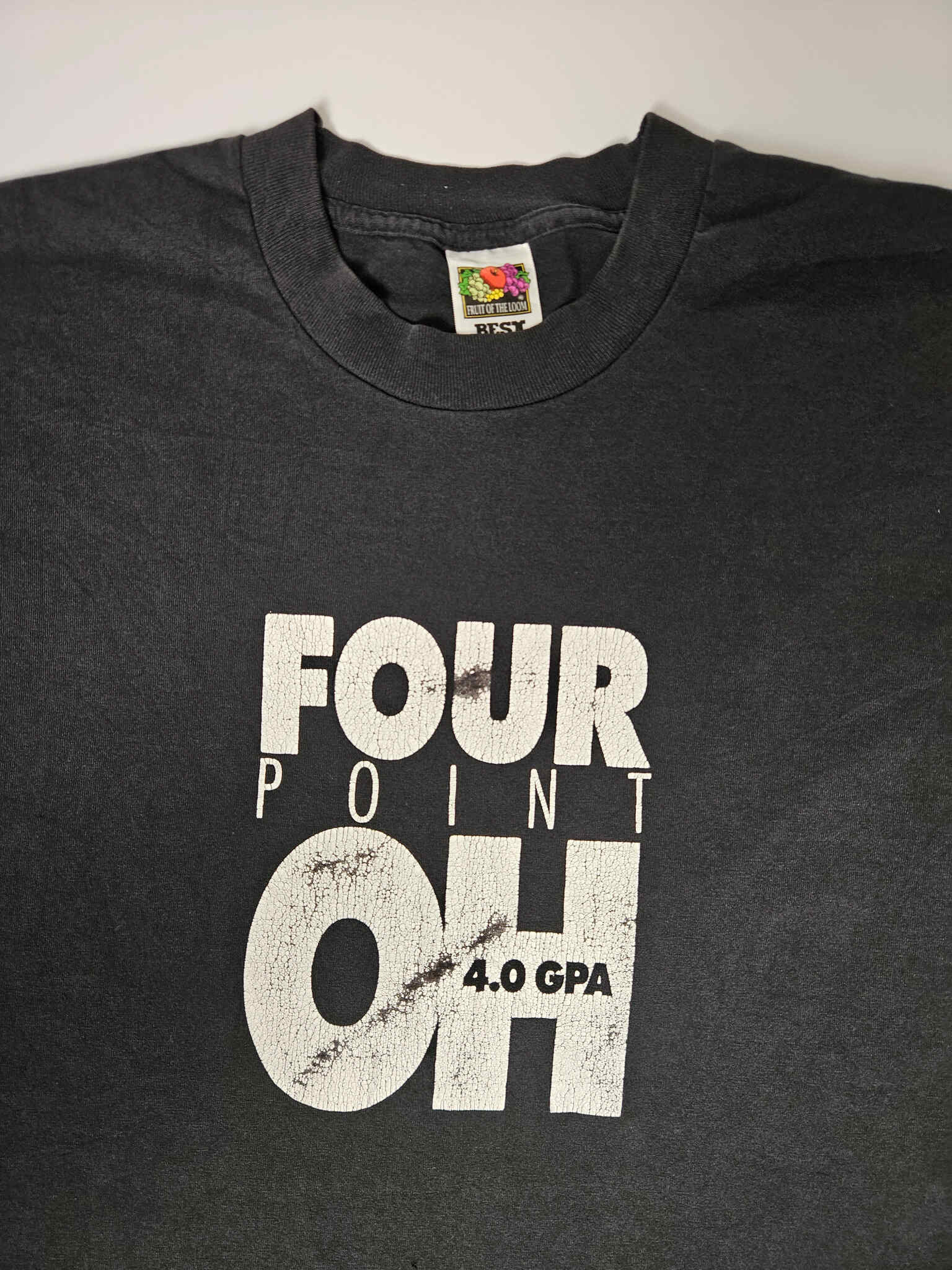 "Voorkant van een zwart vintage T-shirt met een opvallende witte distressed print 'FOUR POINT OH 4.0 GPA'. De tekst heeft een verweerde look die bijdraagt aan de vintage uitstraling. Een perfect voorbeeld van een uniek, pre-loved item binnen de slow fashion collectie."

