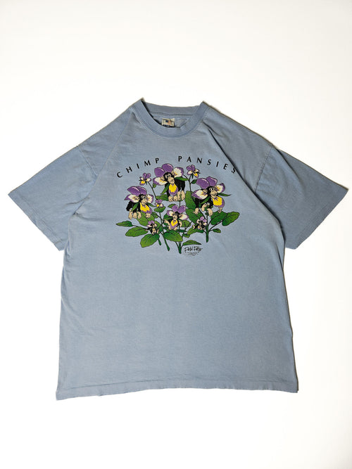 "Lichtblauw vintage T-shirt plat gelegd, met een unieke grafische print van chimpansees die uit paarse en gele bloemen (viooltjes) komen, met de tekst 'CHIMP PANSIES' erboven. Dit speelse en authentieke ontwerp maakt het een perfect voorbeeld van een duurzaam 'slow fashion' statement T-shirt."

