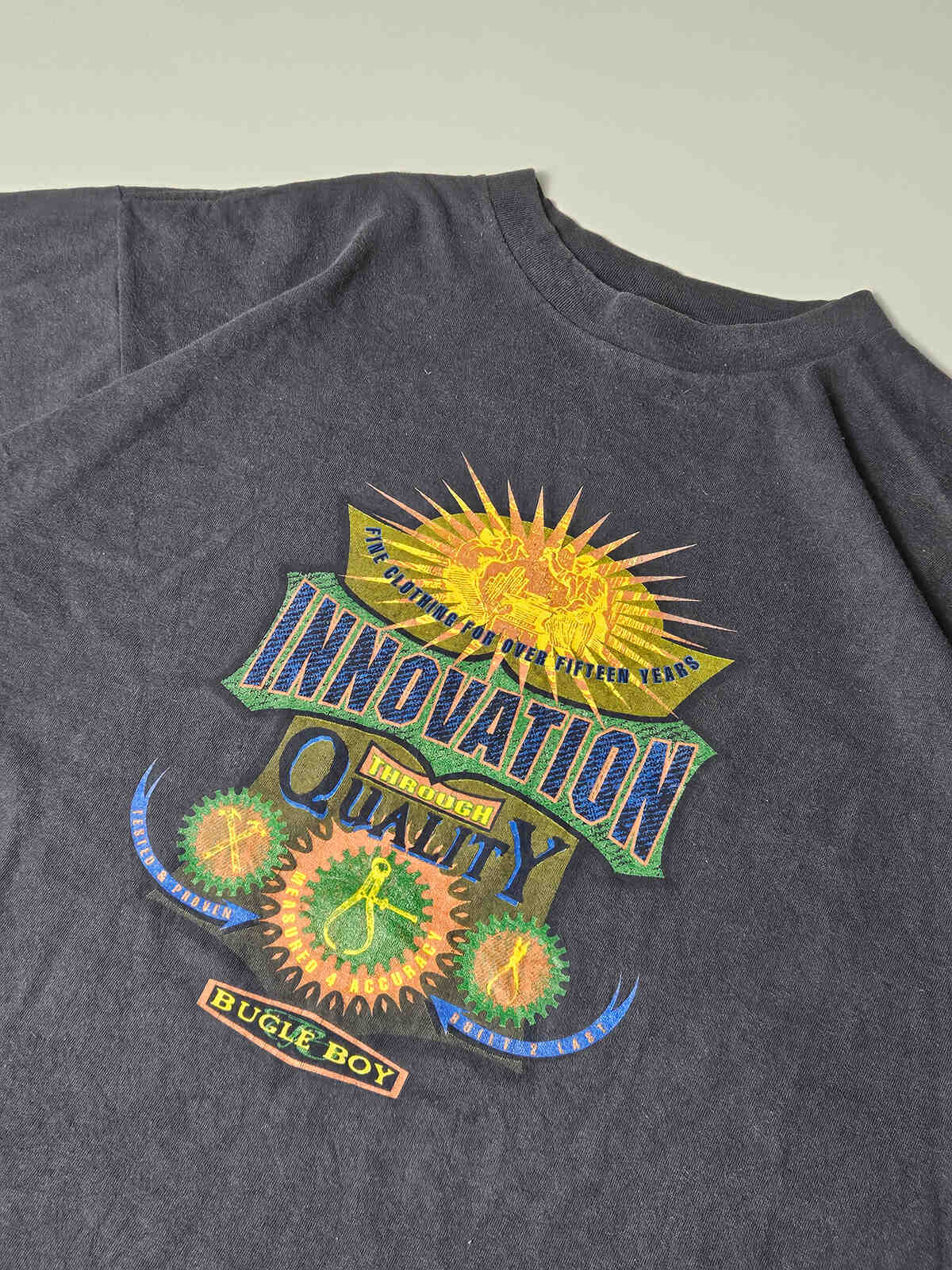 Close-up van 'Innovation Through Quality' print met opvallende zon- en tandwielgrafics – typische jaren 90 plastisol-inkt met subtiele vintage craquelé en natuurlijke patina