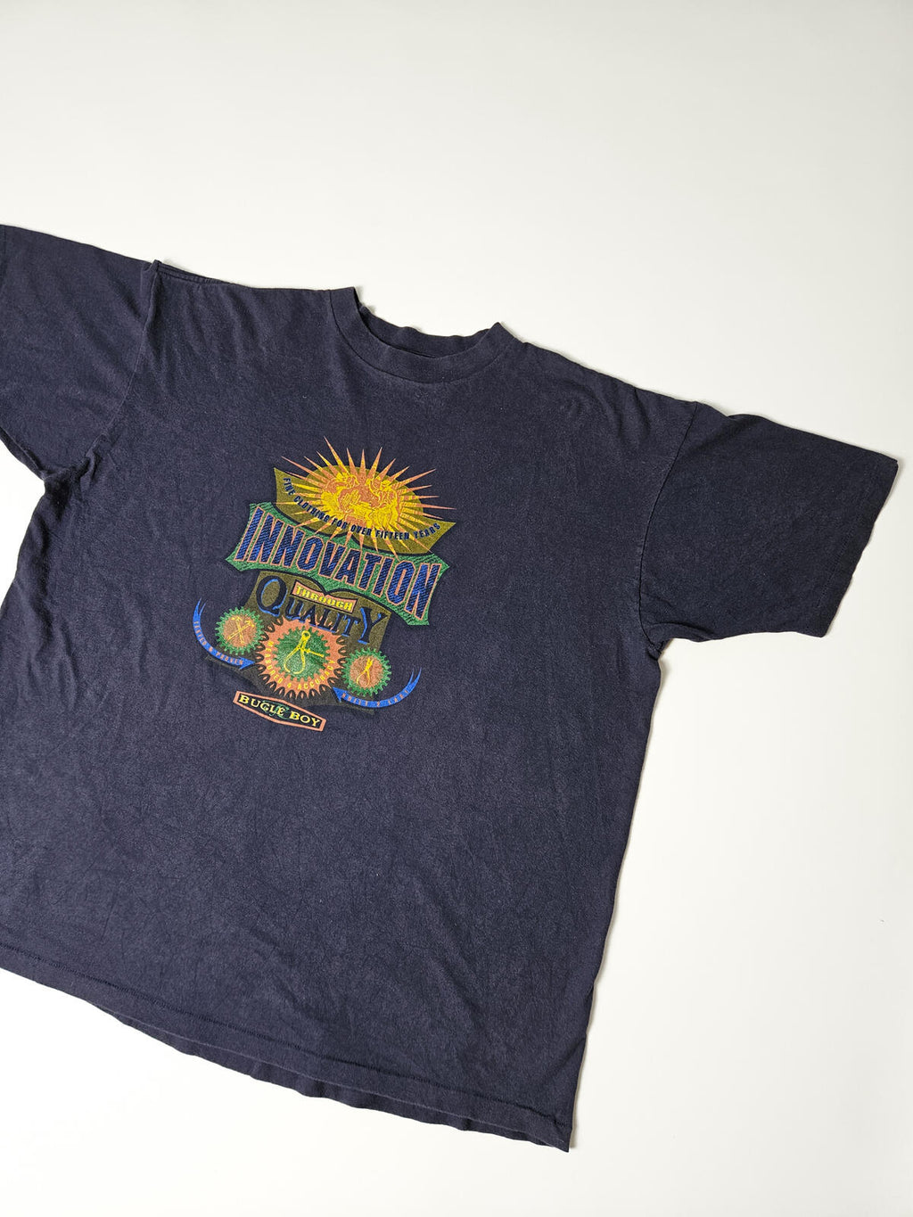 Jaren 90 vintage Bugle Boy T-shirt met kleurrijke 'Innovation Through Quality' grafische opdruk en retro workwear-stijl – populair bij streetwear en 90s collectors