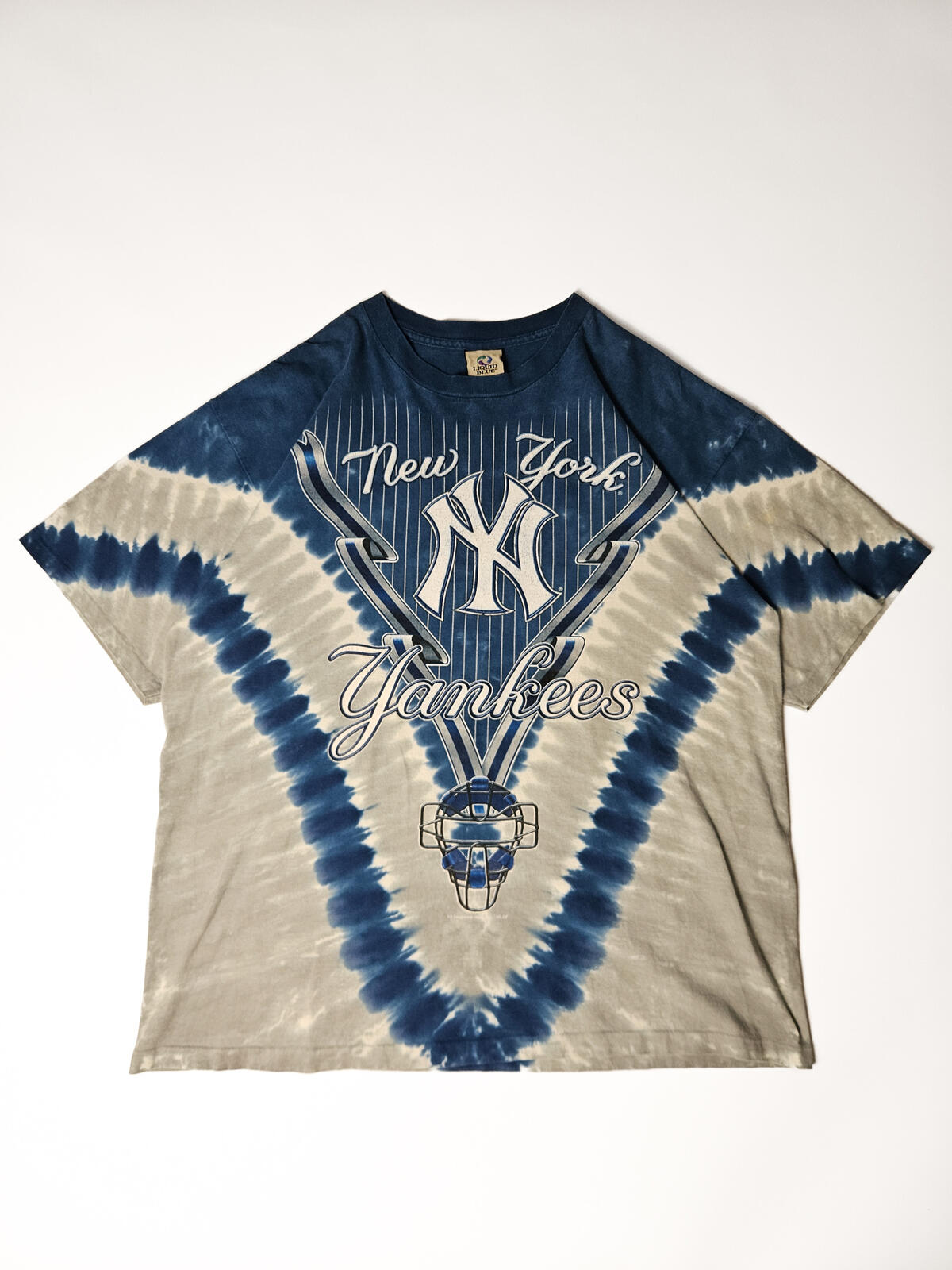 "Vintage New York Yankees tie-dye T-shirt met iconisch pinstripe logo en catcher-masker print – jaren 90 stijl, populair onder MLB fans en vintage streetwear verzamelaars"

