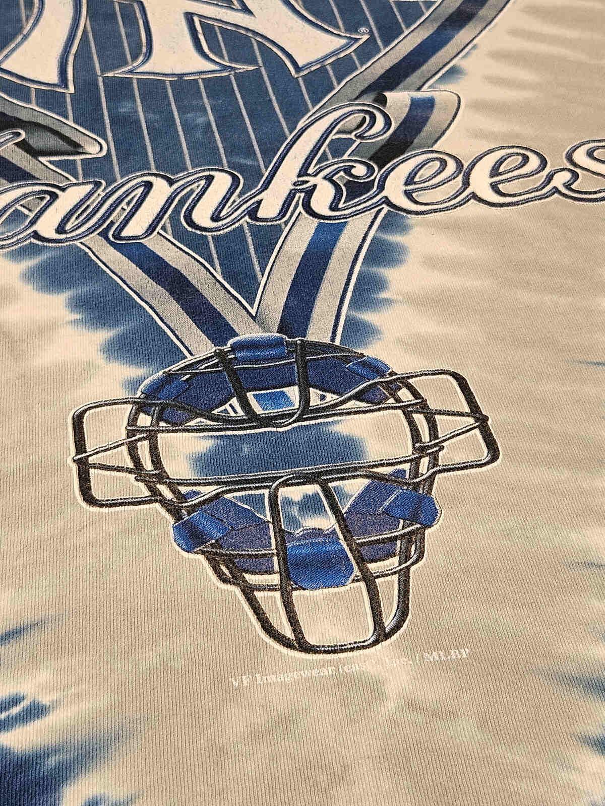 "Close-up van Yankees plastisol-print met subtiele vintage craquelé en tie-dye patroon – typisch jaren 90 MLB merchandise, geliefd bij verzamelaars"

