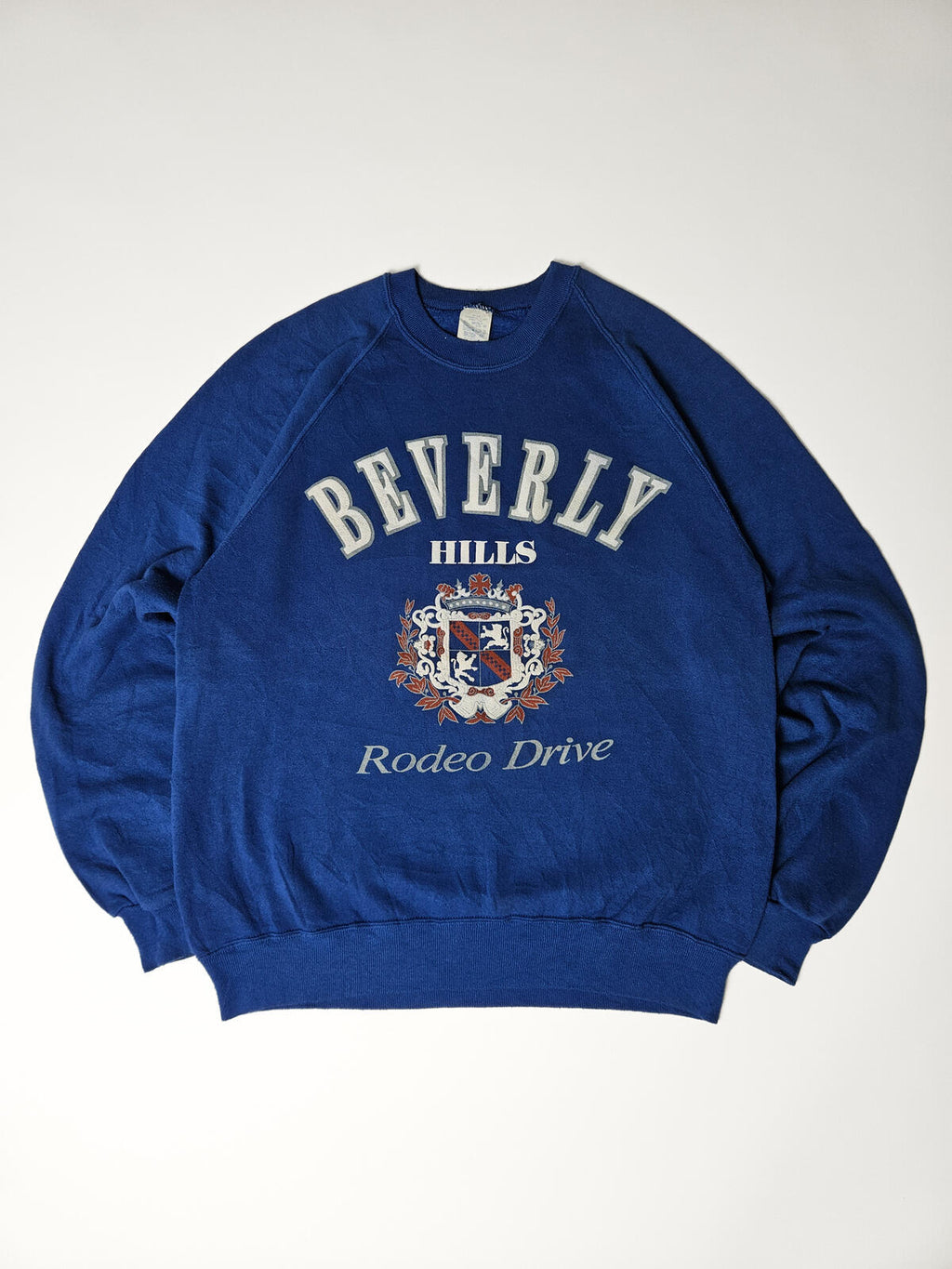 "Vintage Beverly Hills Rodeo Drive sweater in koningsblauw met groot crest logo – klassieke preppy Amerikaanse stijl, populair bij 90s streetwear en resortwear liefhebbers"

