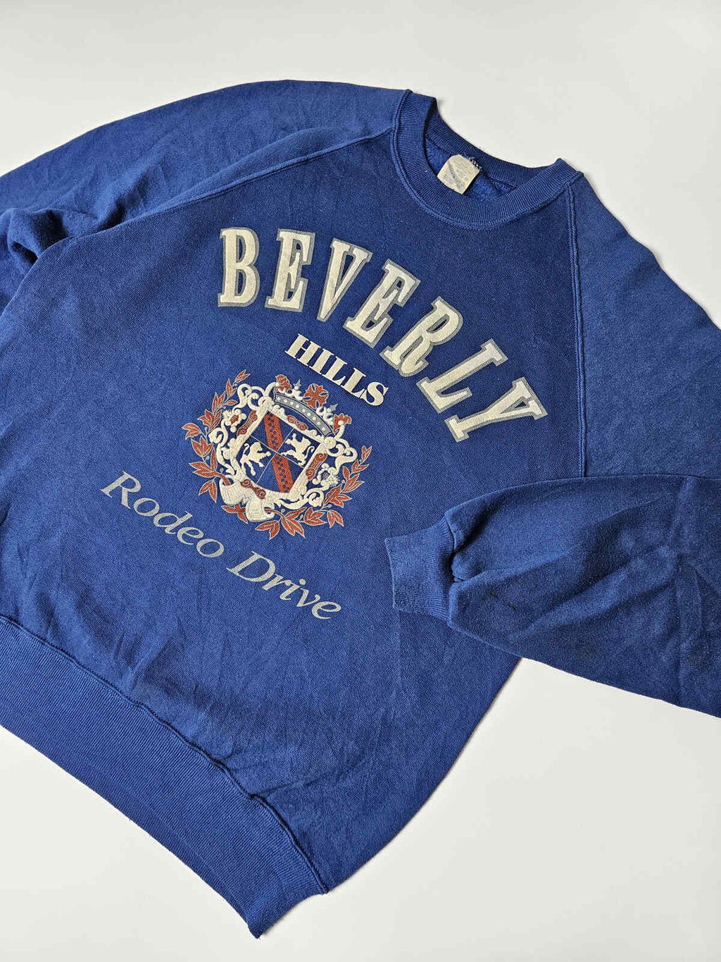 "Blauwe vintage Beverly Hills sweater met geborduurd stijlvol wapen en Rodeo Drive tekst – typisch 80s/90s toeristische preppy fashion"

