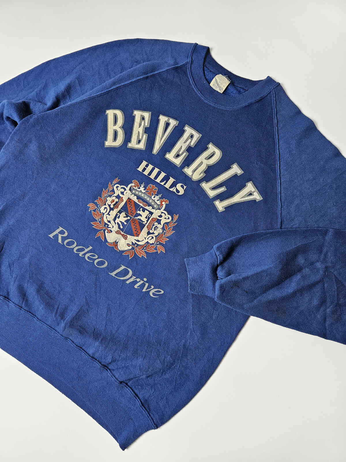 "Blauwe vintage Beverly Hills sweater met geborduurd stijlvol wapen en Rodeo Drive tekst – typisch 80s/90s toeristische preppy fashion"

