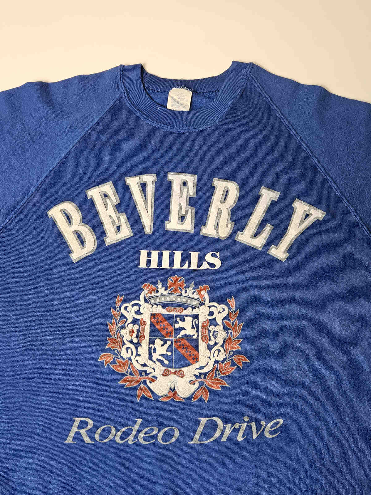 "Close-up van Beverly Hills Rodeo Drive crest op vintage sweater – originele jaren 90 screen printed graphic met lichte natuurlijke slijtage"

