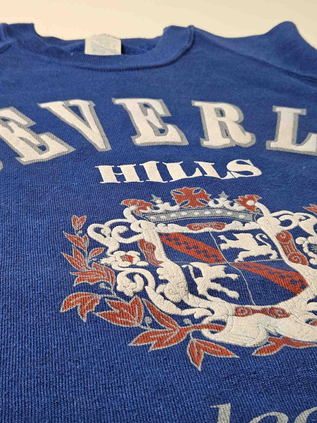 "Close-up van het Beverly Hills wapen met authentieke vintage craquelé en zachte fleece stof – iconisch item voor resortwear en preppy collectors"

