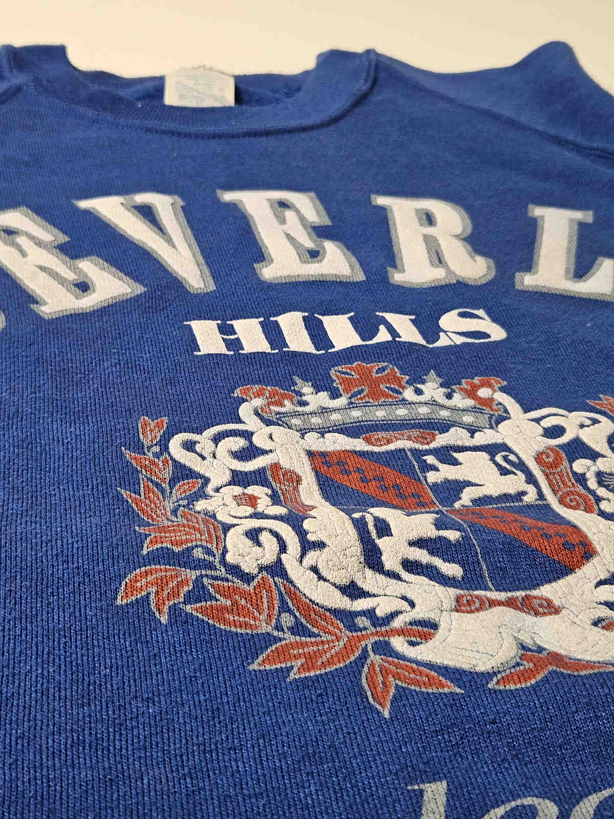 "Close-up van het Beverly Hills wapen met authentieke vintage craquelé en zachte fleece stof – iconisch item voor resortwear en preppy collectors"

