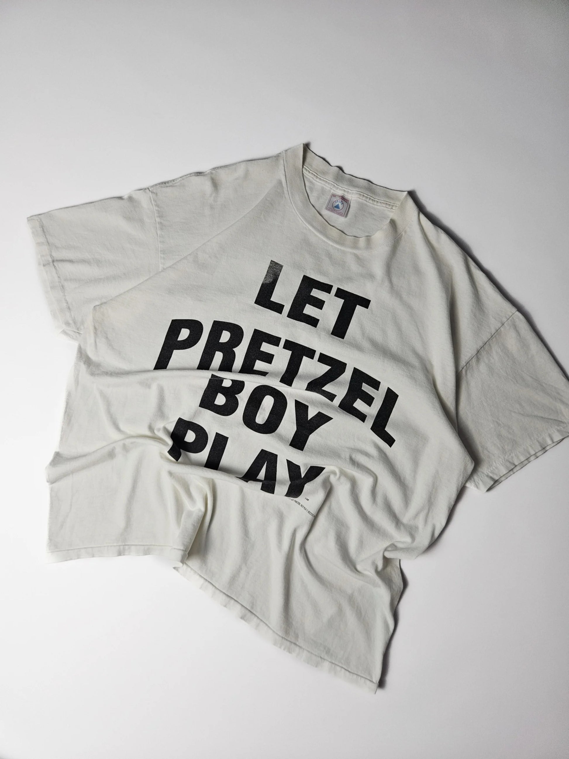 Authentiek 1996 vintage Delta Let Pretzel Boy Play T-shirt in wit met grote zwarte typografische print – single stitch Made in USA, geliefd bij streetwear en reclame T-shirt verzamelaars

