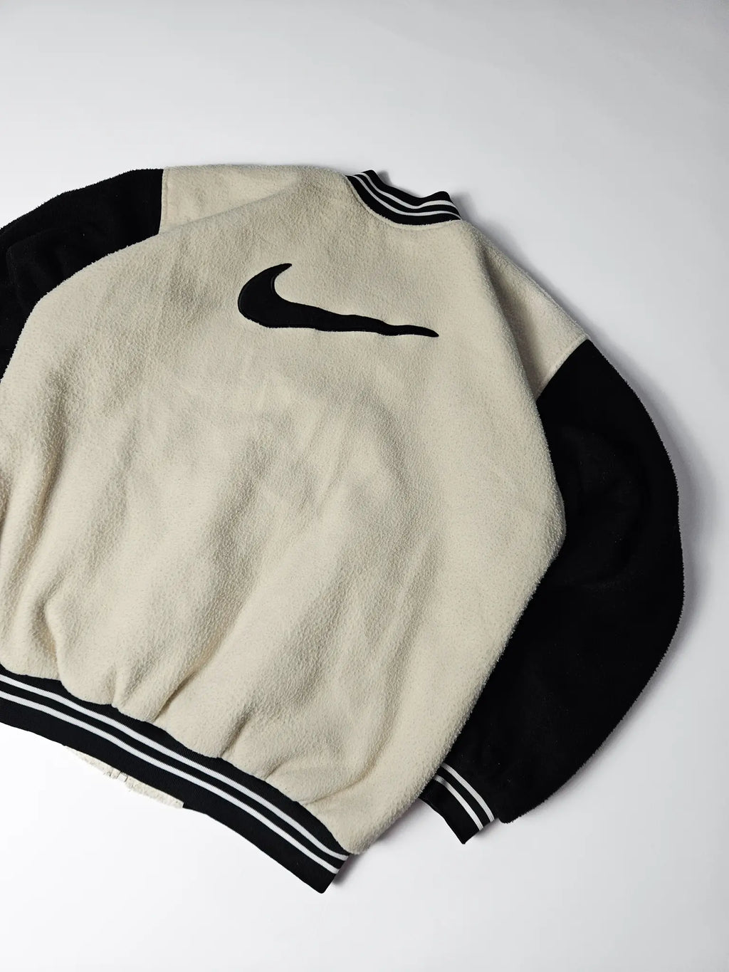 Close-up van groot zwart Nike swoosh logo op beige fleece rug – iconisch jaren 90 varsity jacket design, populair bij streetwear en sportverzamelaars

