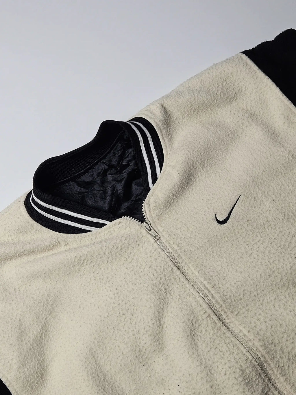 Close-up van beige fleece textuur en zwart geborduurd Nike swoosh logo – jaren 90 vintage varsity jacket, zeldzaam retro sport streetwear

