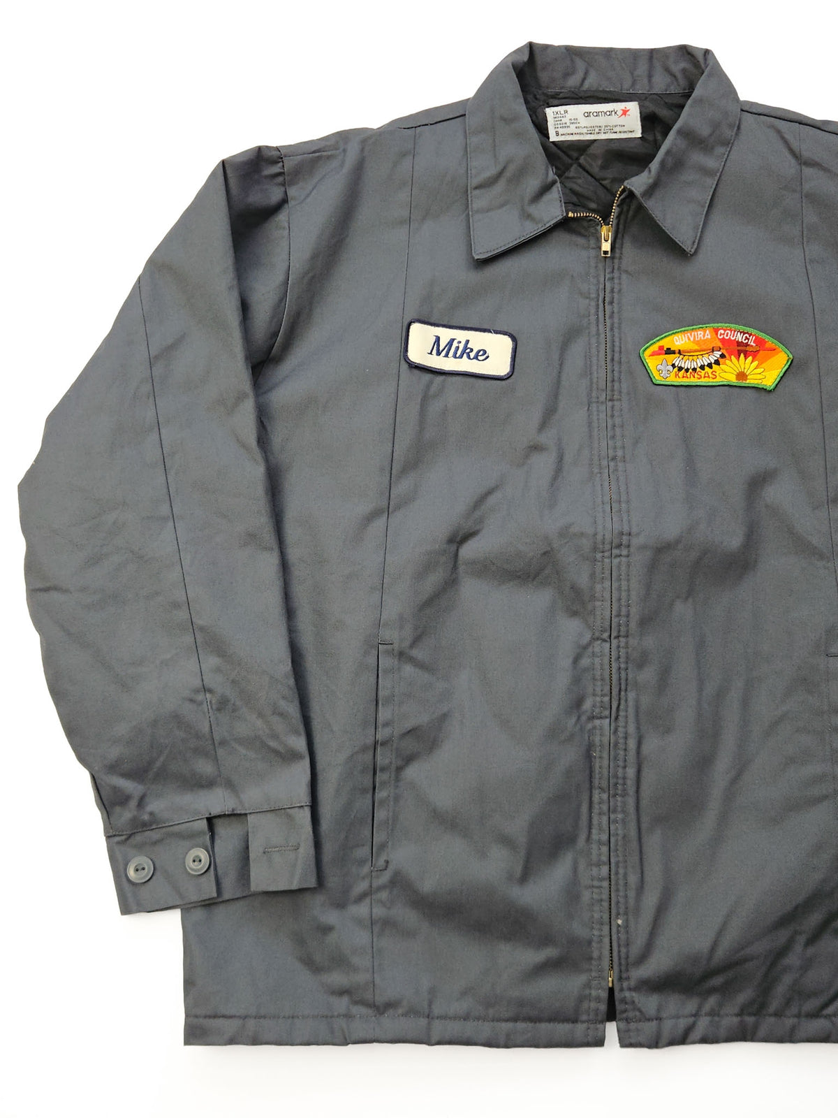 Donkergrijze vintage Aramark workwear jas uit de jaren 90 met Mike-naamlabel en Quivira Council Kansas-patch, voorzijde als flatlay.