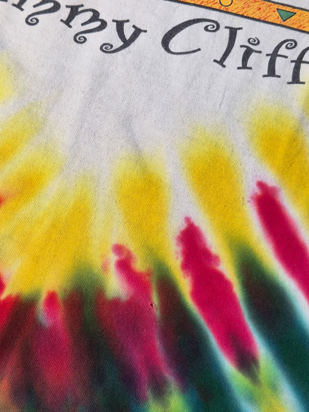 Kleine pinhole aan de voorkant van een vintage Jimmy Cliff World Tour tie-dye T-shirt uit 1995.