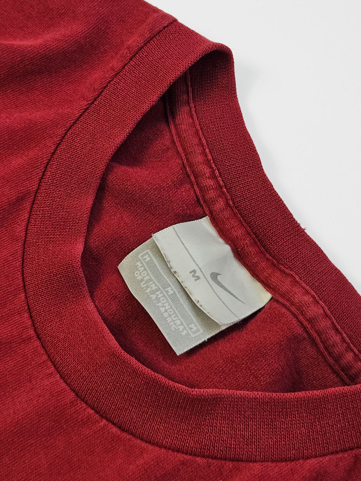 Wit Nike-neklabel met grijze swoosh en maataanduiding M aan de binnenkant van de rode hals.