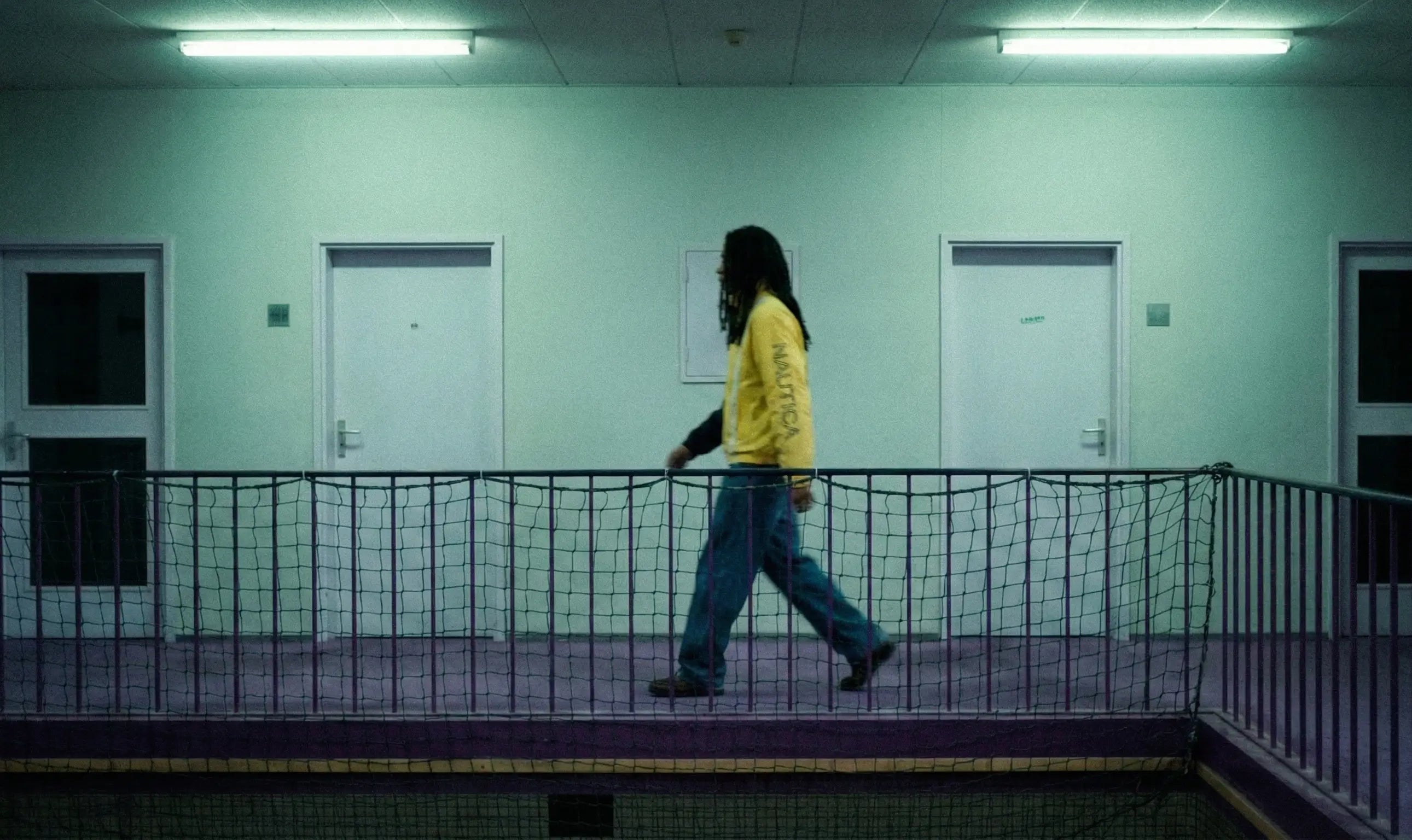 Model wearing a vintage Nautica jacket by Slow Fashion Vintage walking along a dim lit school in the Netherlands