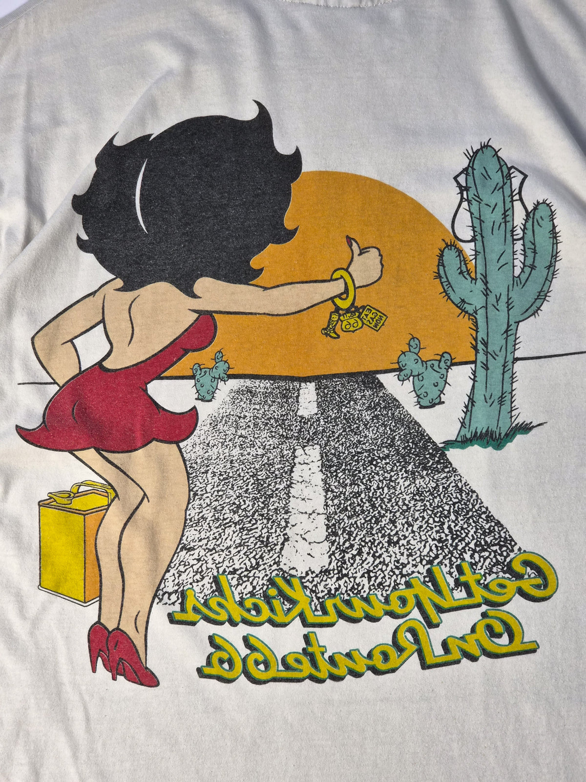 Detail van een ecru Betty Boop vintage T-shirt uit de jaren '90 met faded Route 66 zeefdruk, kleine vlekjes en zichtbare gebruikssporen.