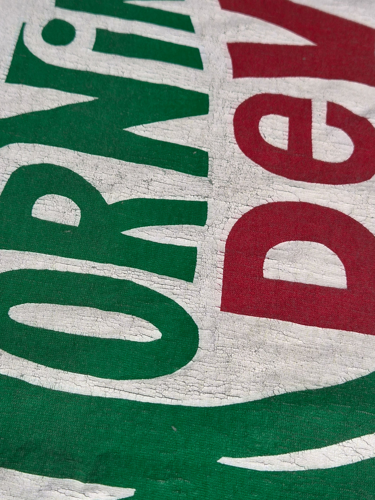 Close-up van de Morning Dew-print met fijne craquelure in het gebroken witte vlak en groene en rode letters.