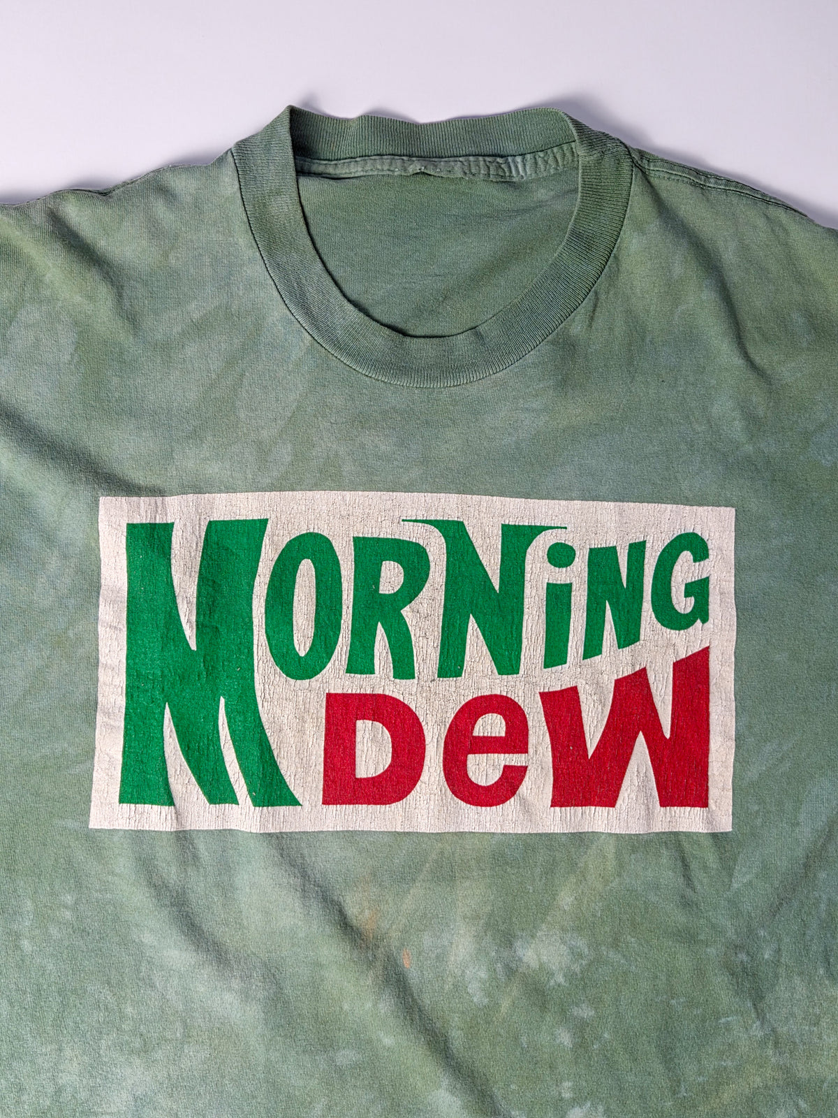 Close-up van de Morning Dew-print met fijne craquelure in het gebroken witte vlak en groene en rode letters.