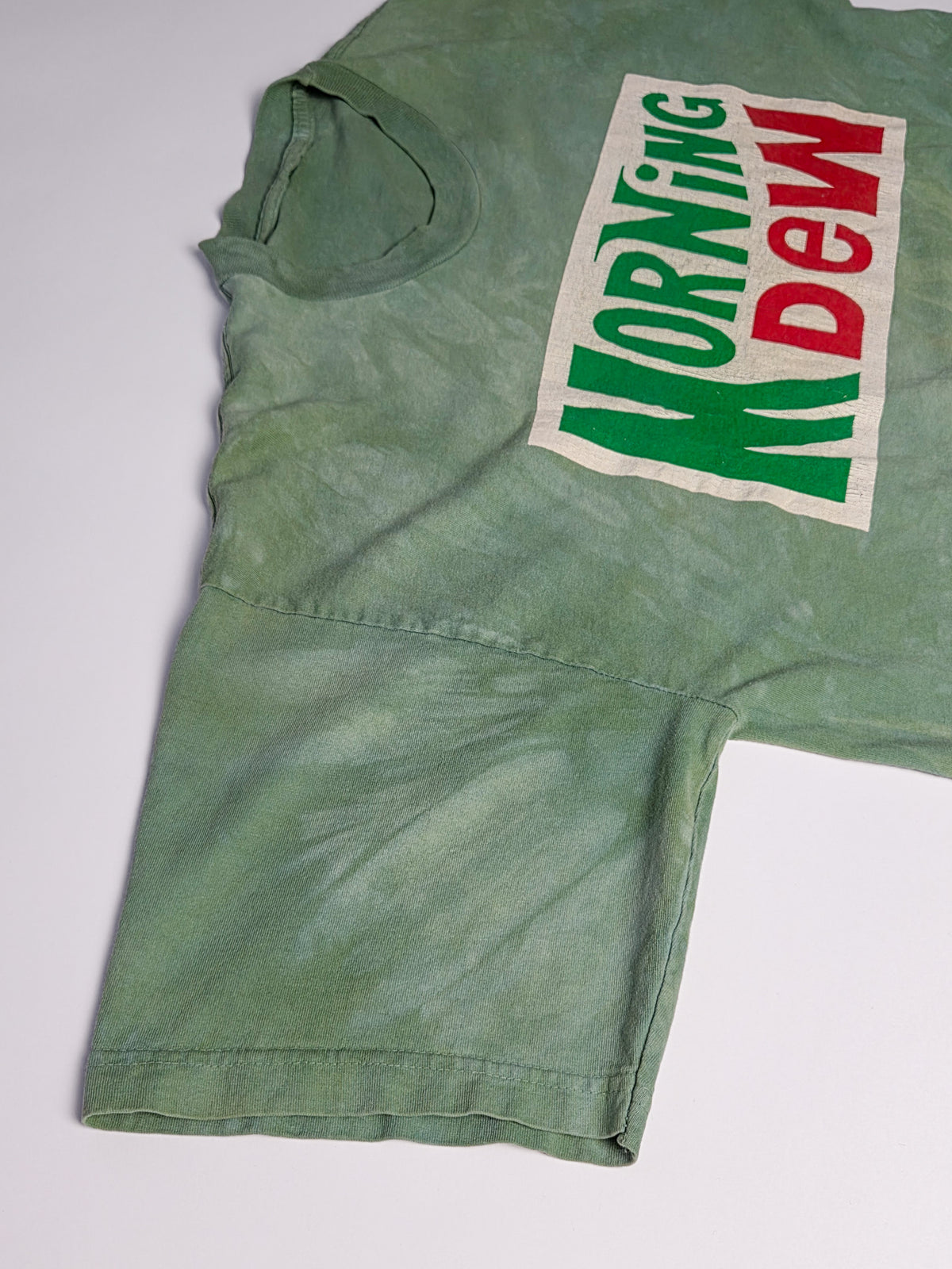 Schuin gefotografeerd Morning Dew T-shirt met grijsgroene fade, ronde hals en dubbel gestikte mouwzoom.