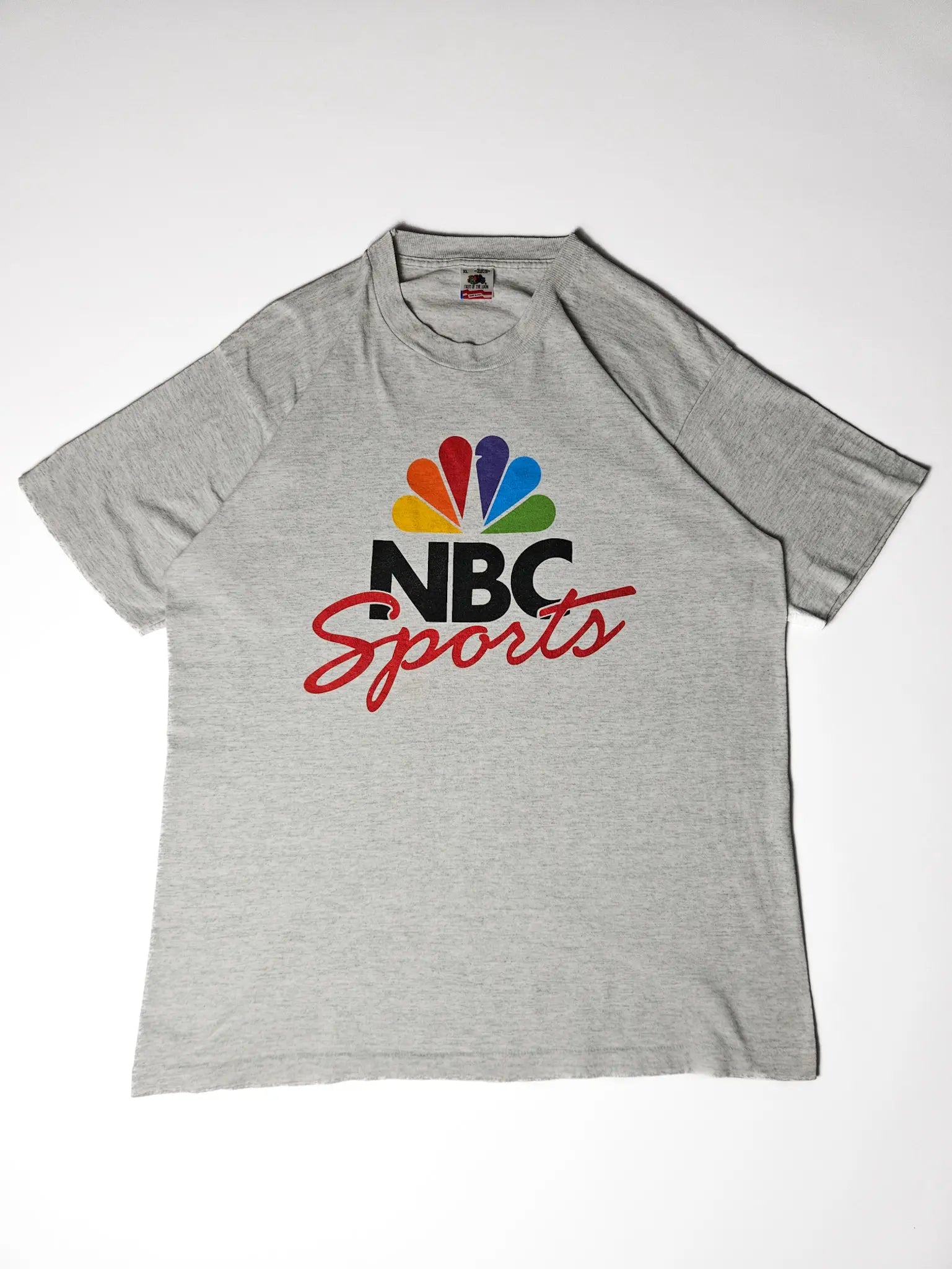 Flatlay: Grijs NBC T-shirt platgelegd met regenboogpauw-graphic

