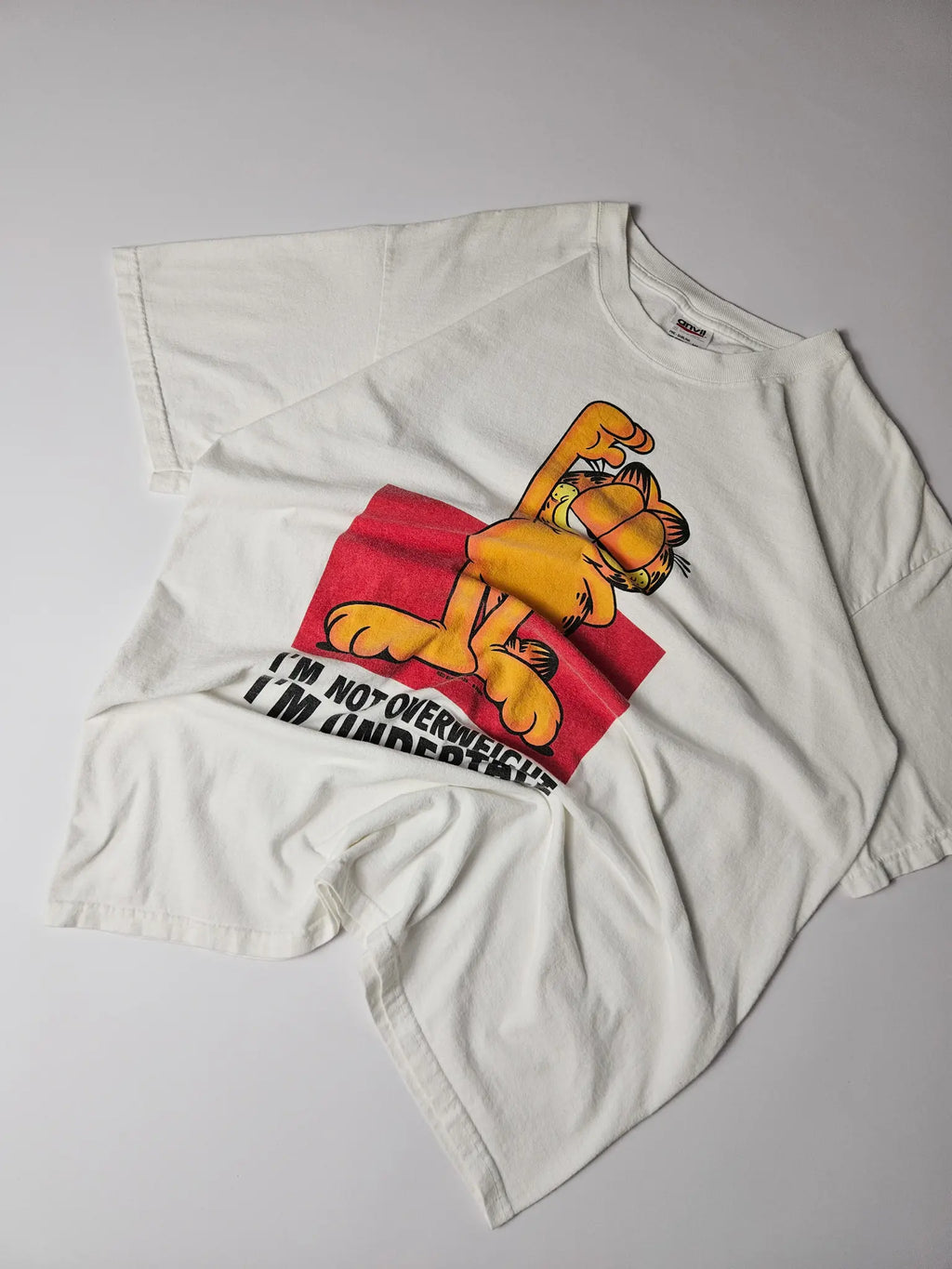 Flatlay: Licht gebroken wit Garfield shirt met kleurrijke frontprint

