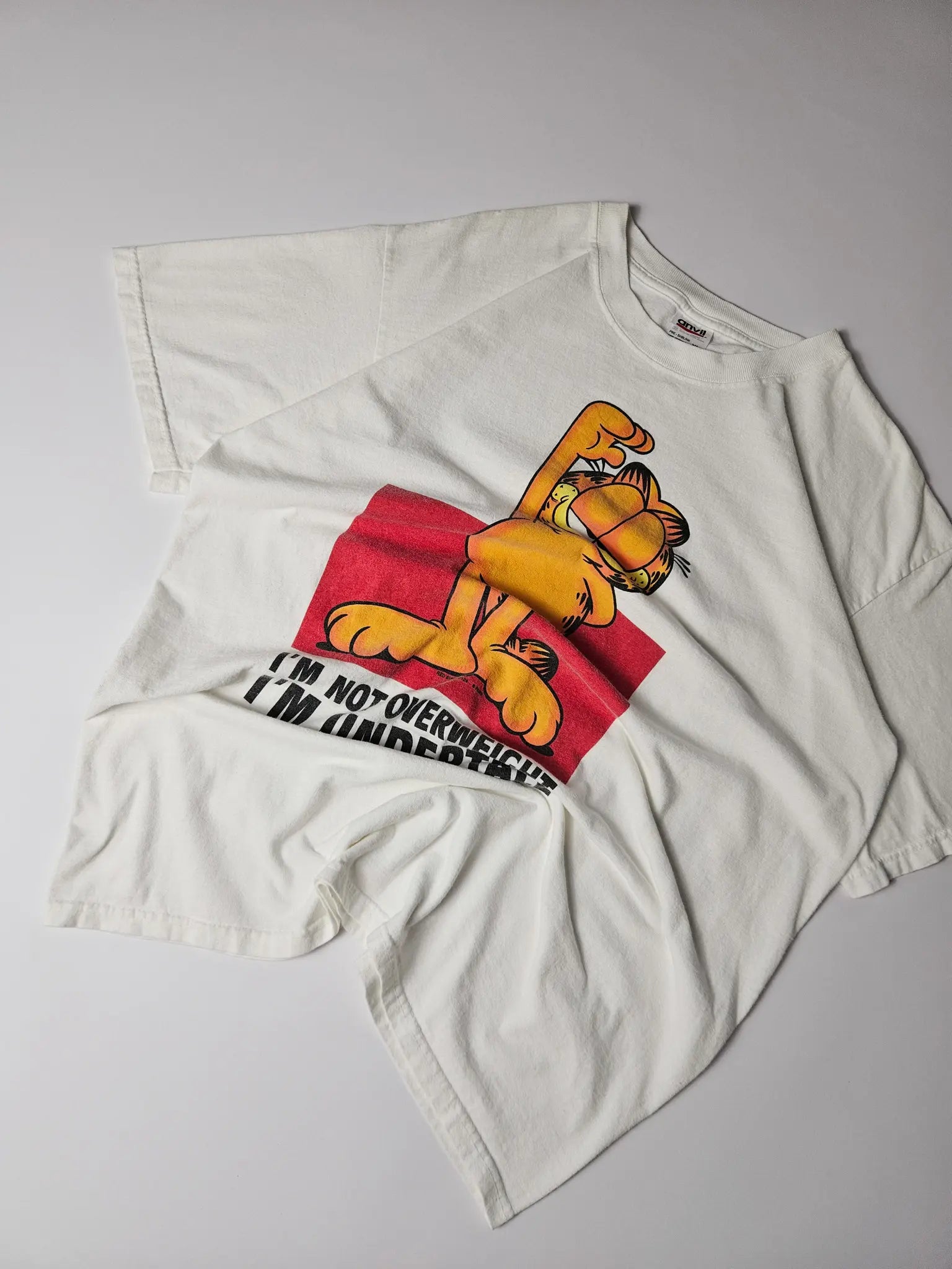 Flatlay: Licht gebroken wit Garfield shirt met kleurrijke frontprint

