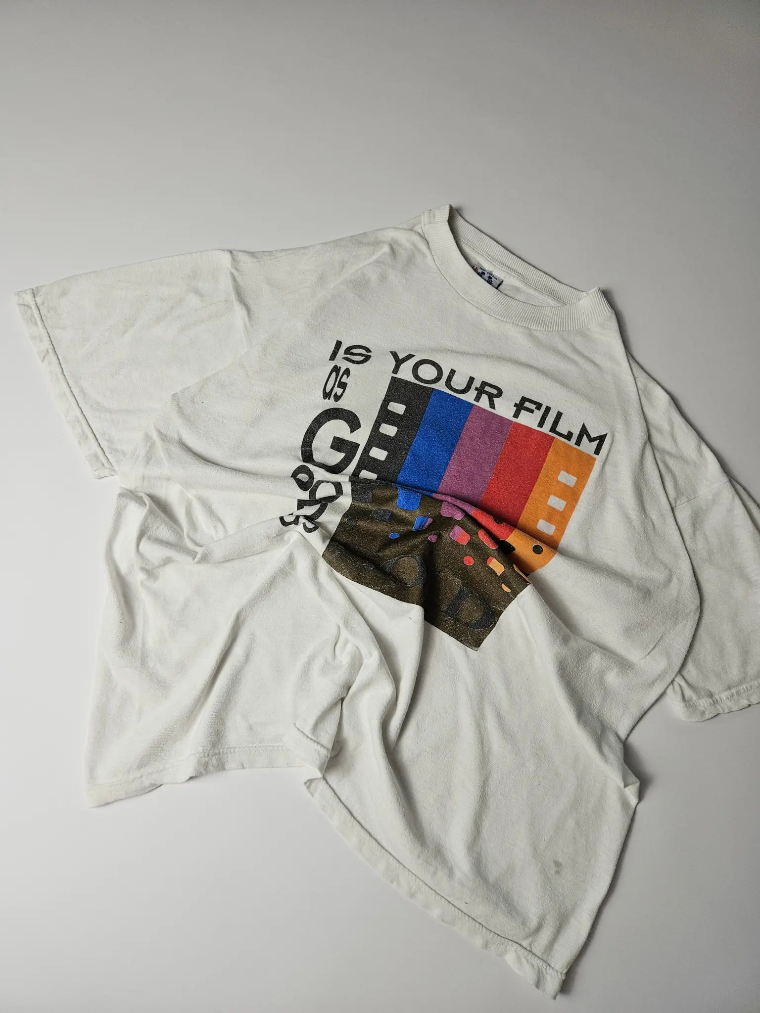 Flatlay: Witte vintage tee platgelegd met kleurrijke fotografieprint

