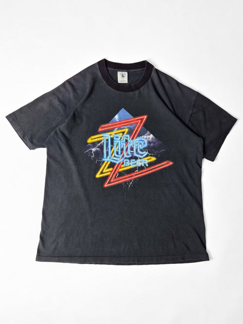 Faded zwart vintage Miller Lite T-shirt met een kleurrijke ZZ Top-neonprint en bliksemschichten op de voorkant.