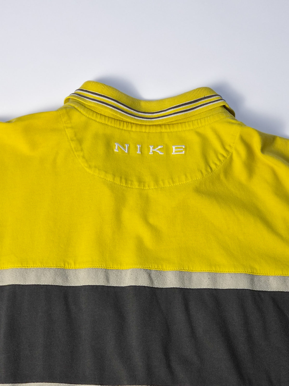 Detail van geel vintage Nike rugby shirt uit de jaren 90 met gestreepte polo collar, colorblock rugpaneel en geborduurd NIKE-logo.