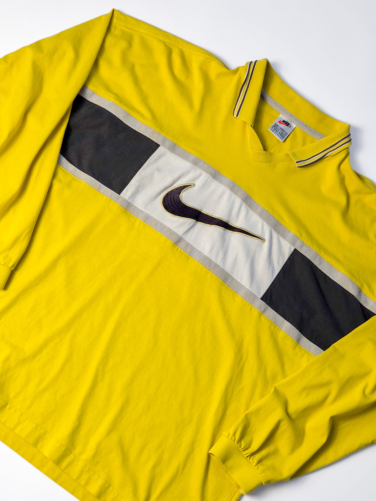 Detail van vintage Nike rugby shirt uit de jaren 90 in geel met zwart-wit borstpaneel en grote geborduurde Center Swoosh.