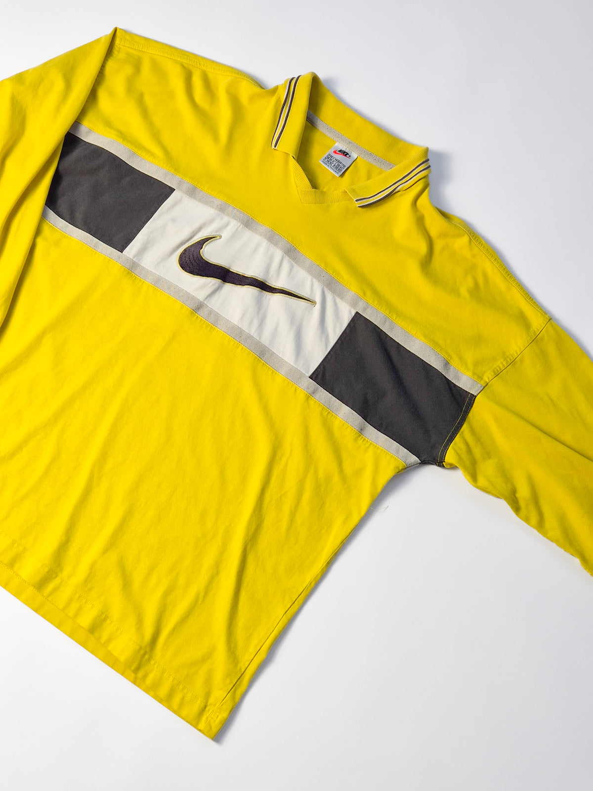 Vintage Nike rugby shirt uit de jaren 90 in geel met zwart-wit colorblock borstpaneel, lange mouwen en grote Center Swoosh.