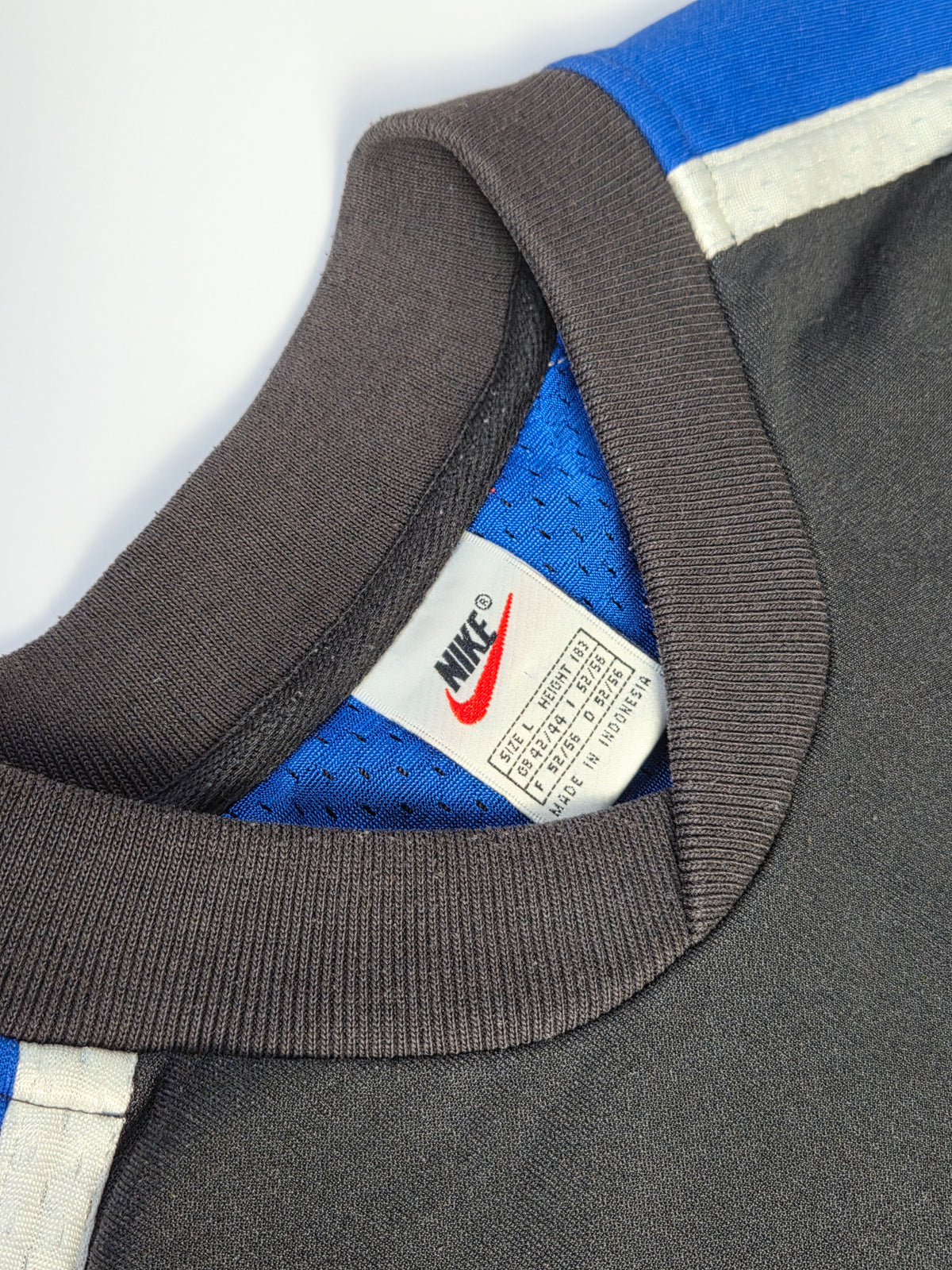 Wit Nike-halslabel met rode Swoosh, maat L en Made in Indonesia boven de blauwe binnenstof.