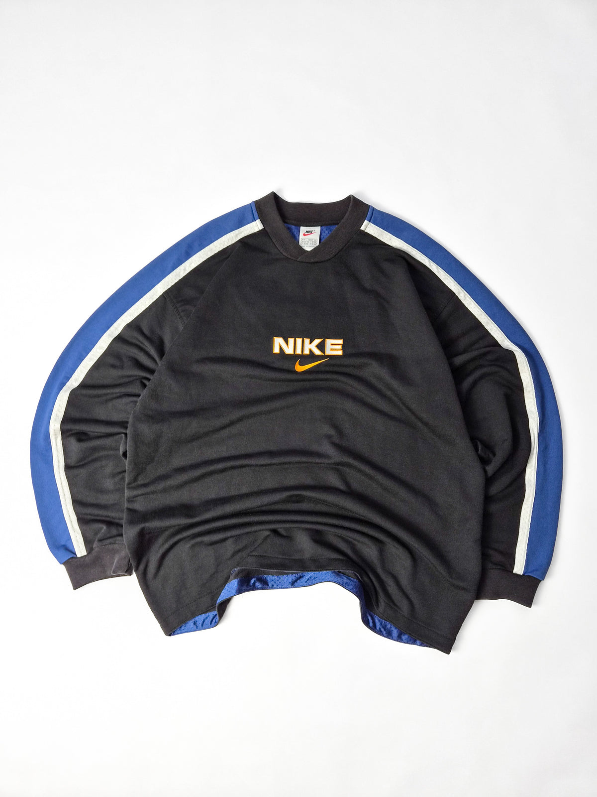 Zwarte vintage Nike sweater met Nike-naam, oranje Swoosh en blauw-witte banen over de schouders en mouwen.