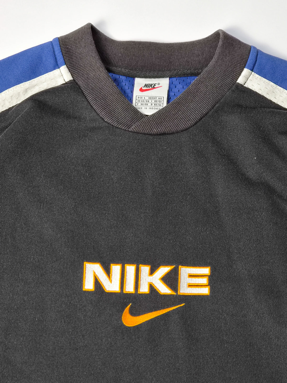Wit Nike-halslabel met rode Swoosh, maat L en Made in Indonesia boven de blauwe binnenstof.