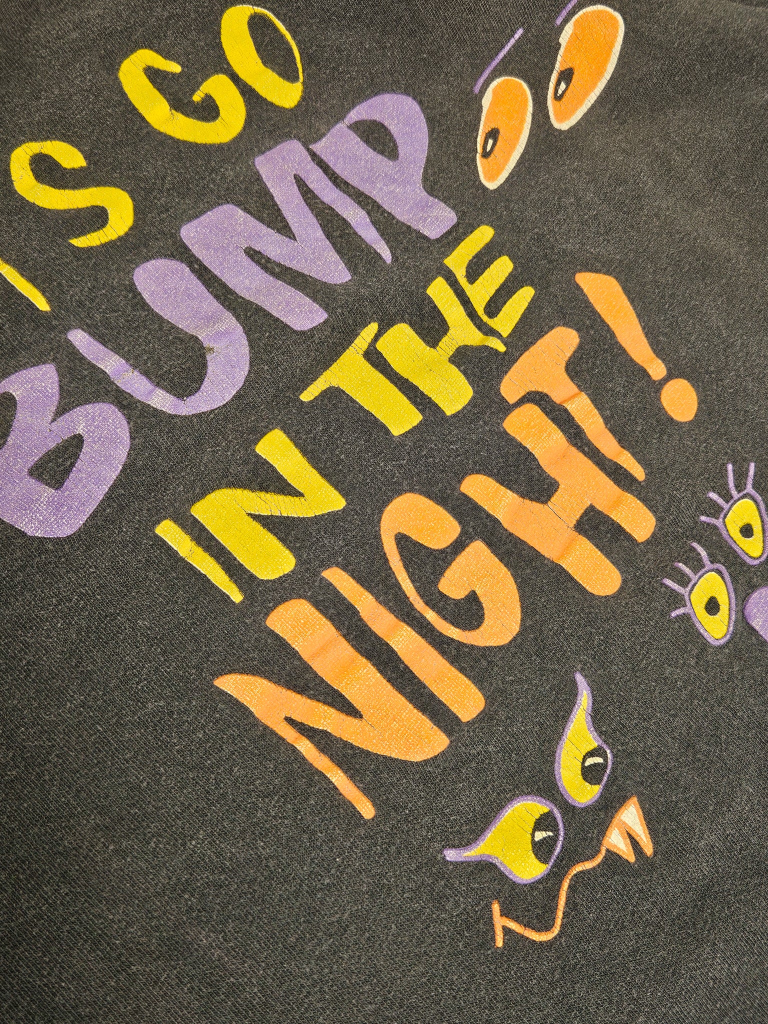 Close-up van de "Let's Go Bump in the Night" print met neonkleuren op vintage T-shirt