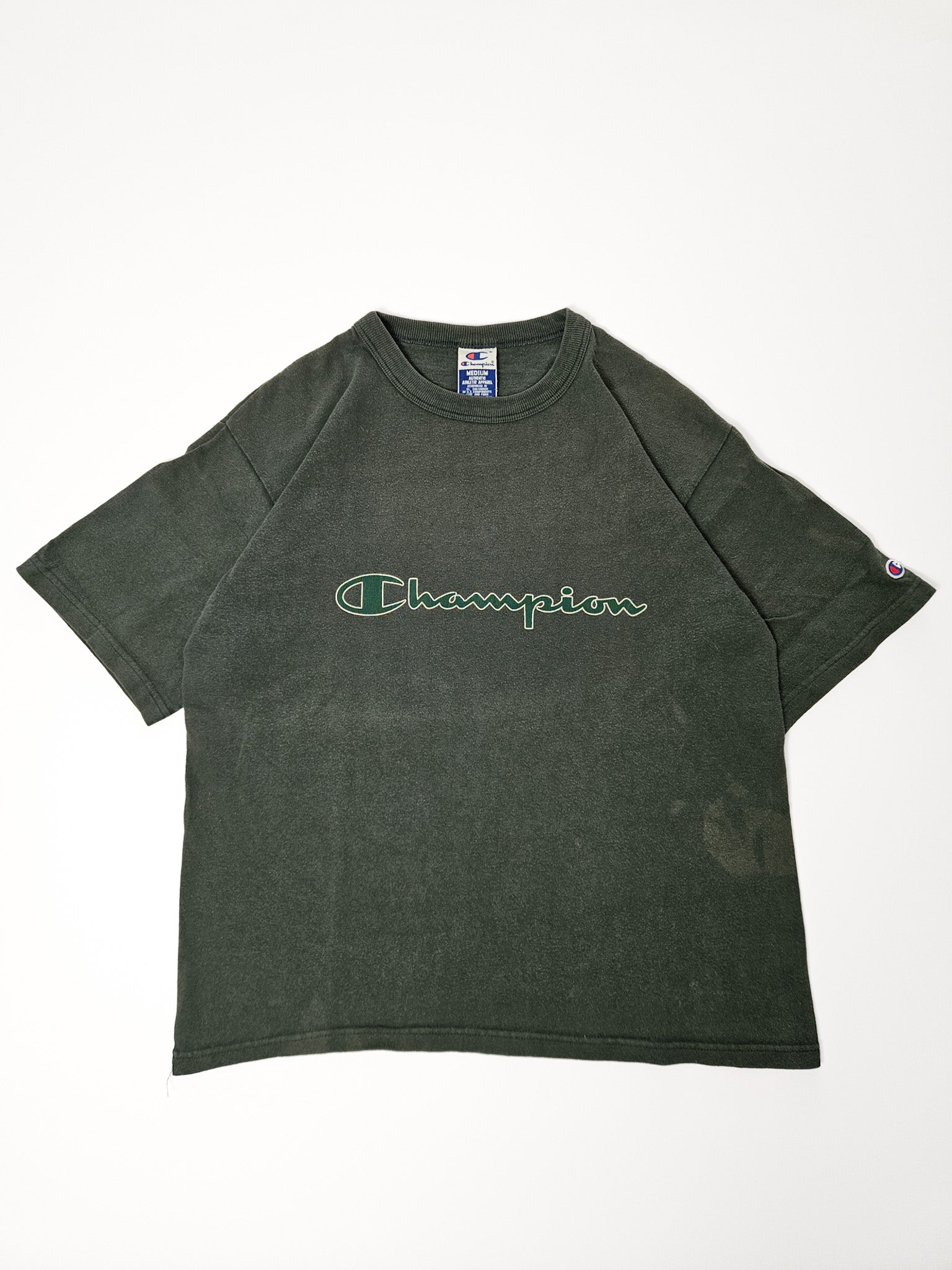 Vooraanzicht van vervaagd groen Champion T-shirt met groot script logo in witte en groene outline
