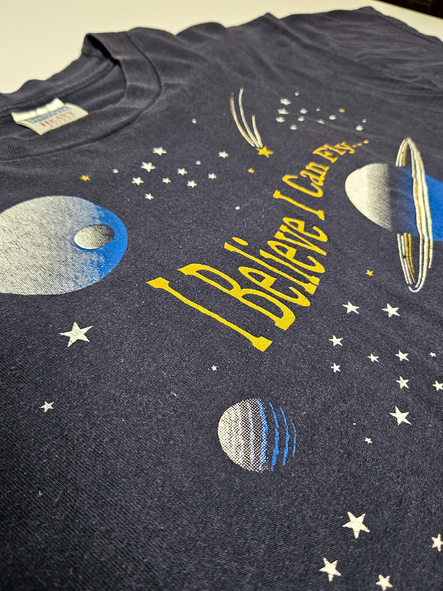 Close-up van de ruimteprint op vintage T-shirt met I Believe I Can Fly tekst en planeten