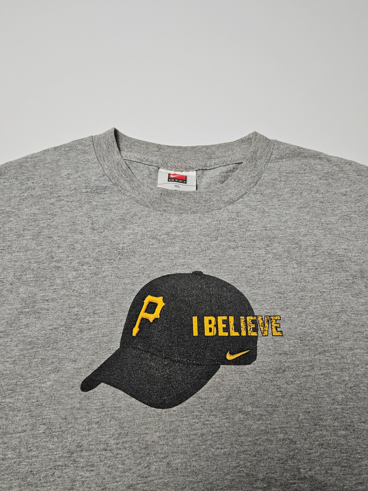 Close-up van de “I BELIEVE” print met gele pet en Nike swoosh
