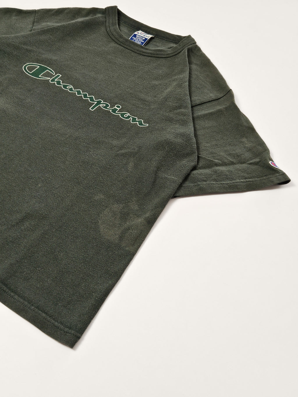 Flatlay van het groene 90s Champion T-shirt met groot script logo en korte mouwen
