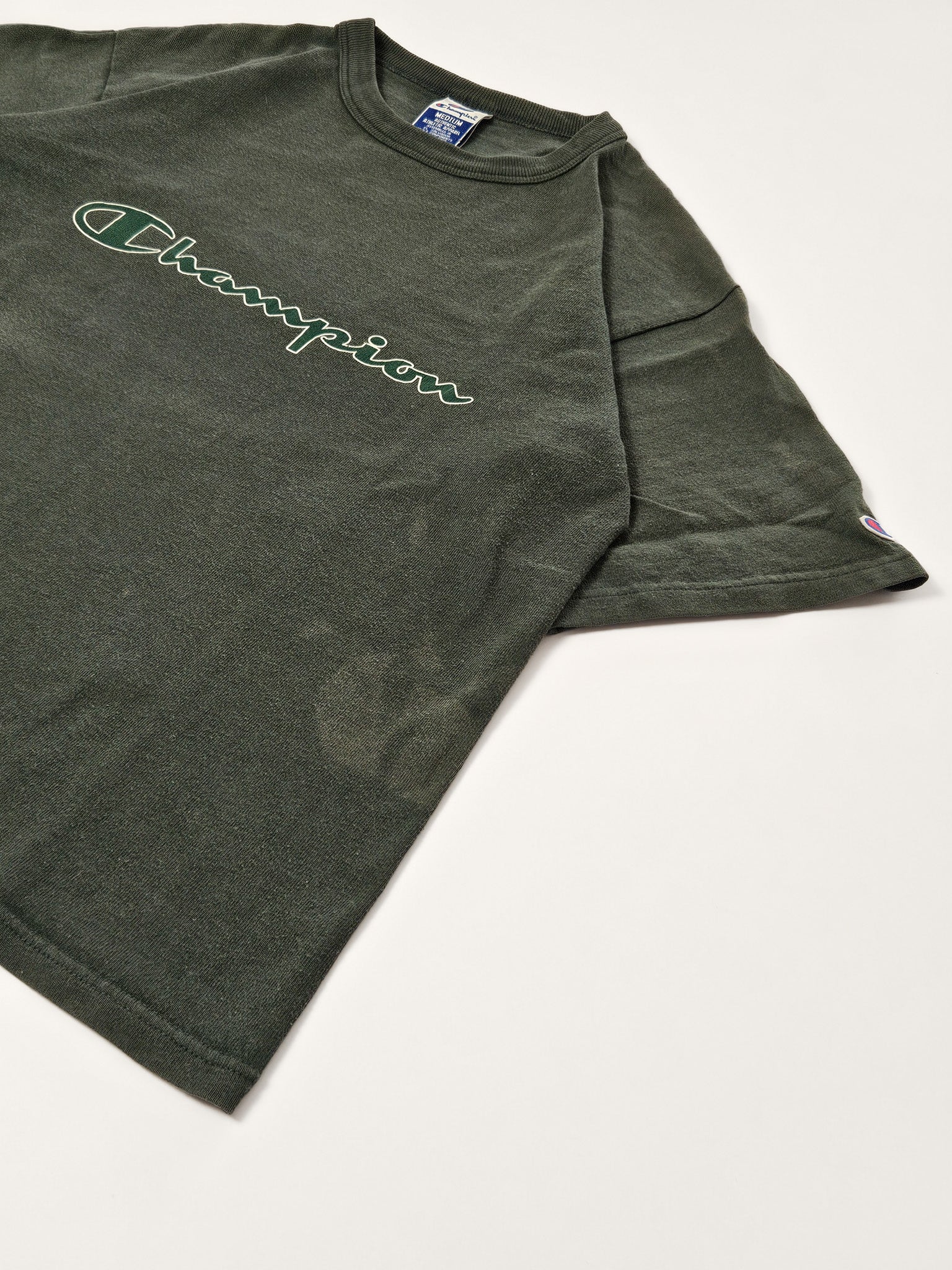 Flatlay van het groene 90s Champion T-shirt met groot script logo en korte mouwen
